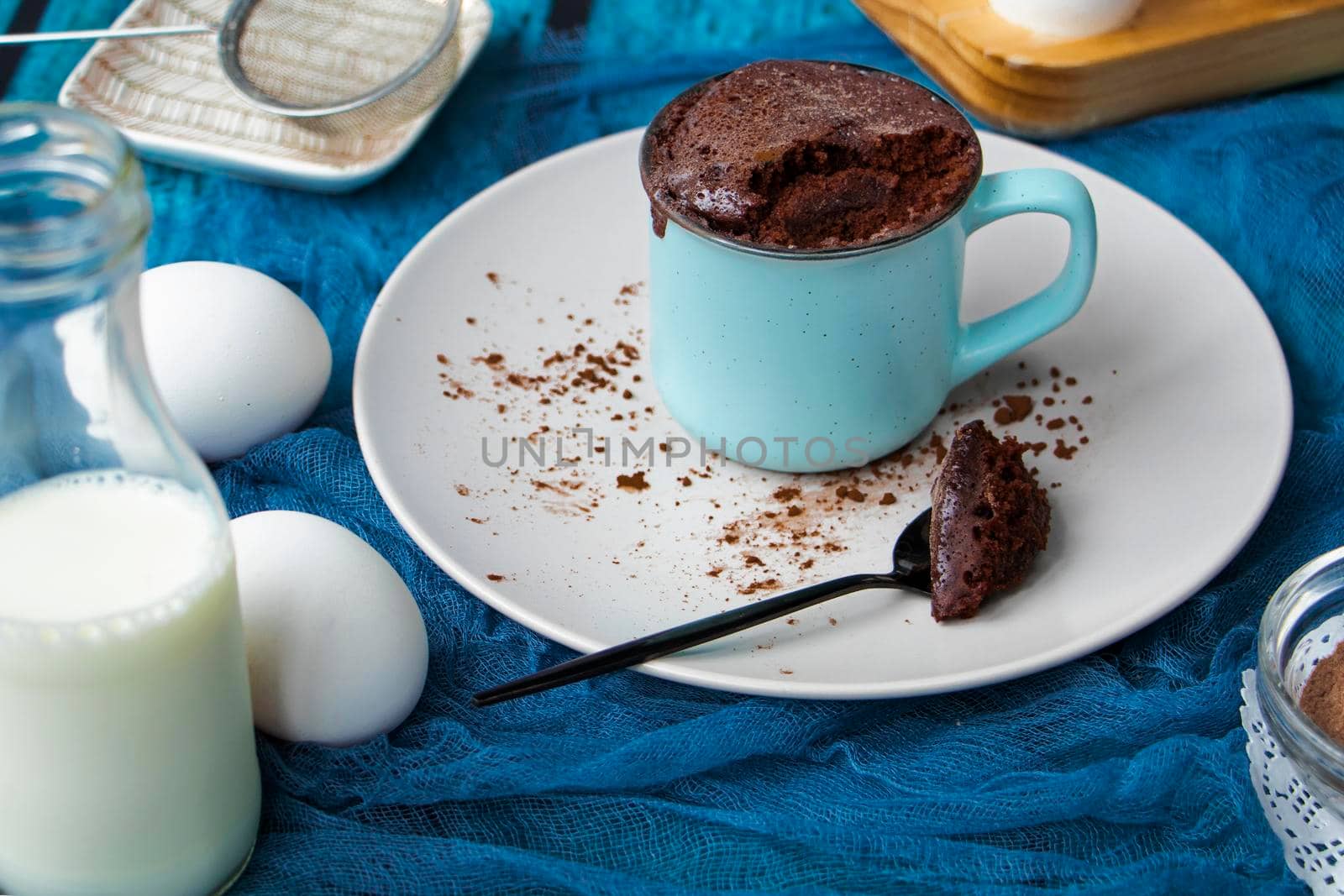 mugcake is microwaved. Homemade cupcake in a mug is on a plate. Chocolate brownie mug cake. Easy cooking concept, microwave baking. muffin chocolate. ingredients, eggs, milk, cocoa.