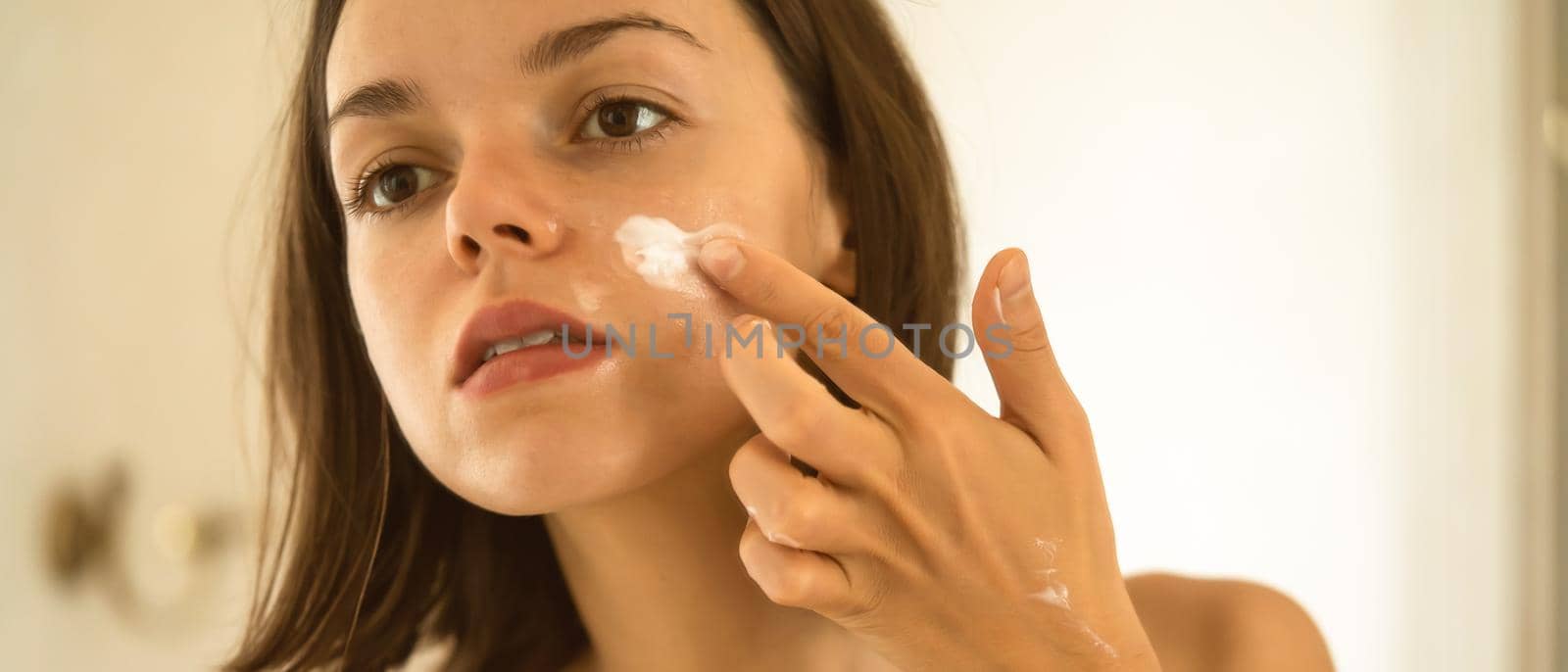 A young girl takes care of the health and beauty of her skin, a woman applies a moisturizing day cream on her face in the bathroom.