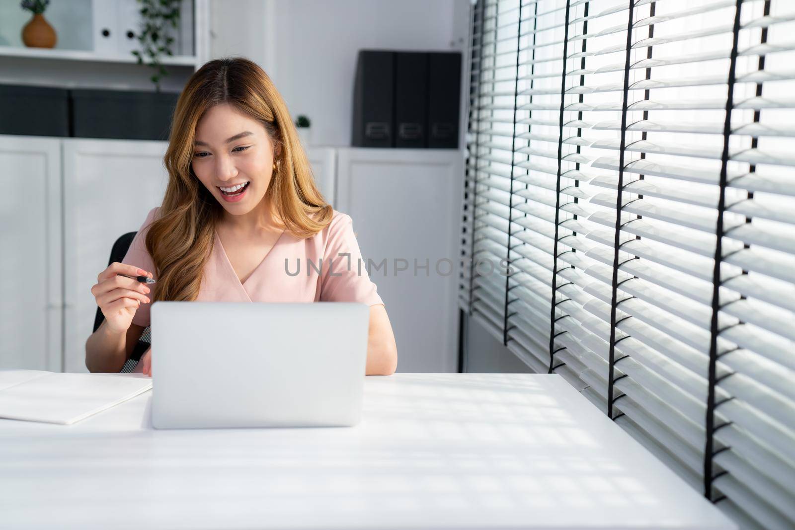 A young Asian female employee sitting at her desk in her office, sitting at desktop in workstation.