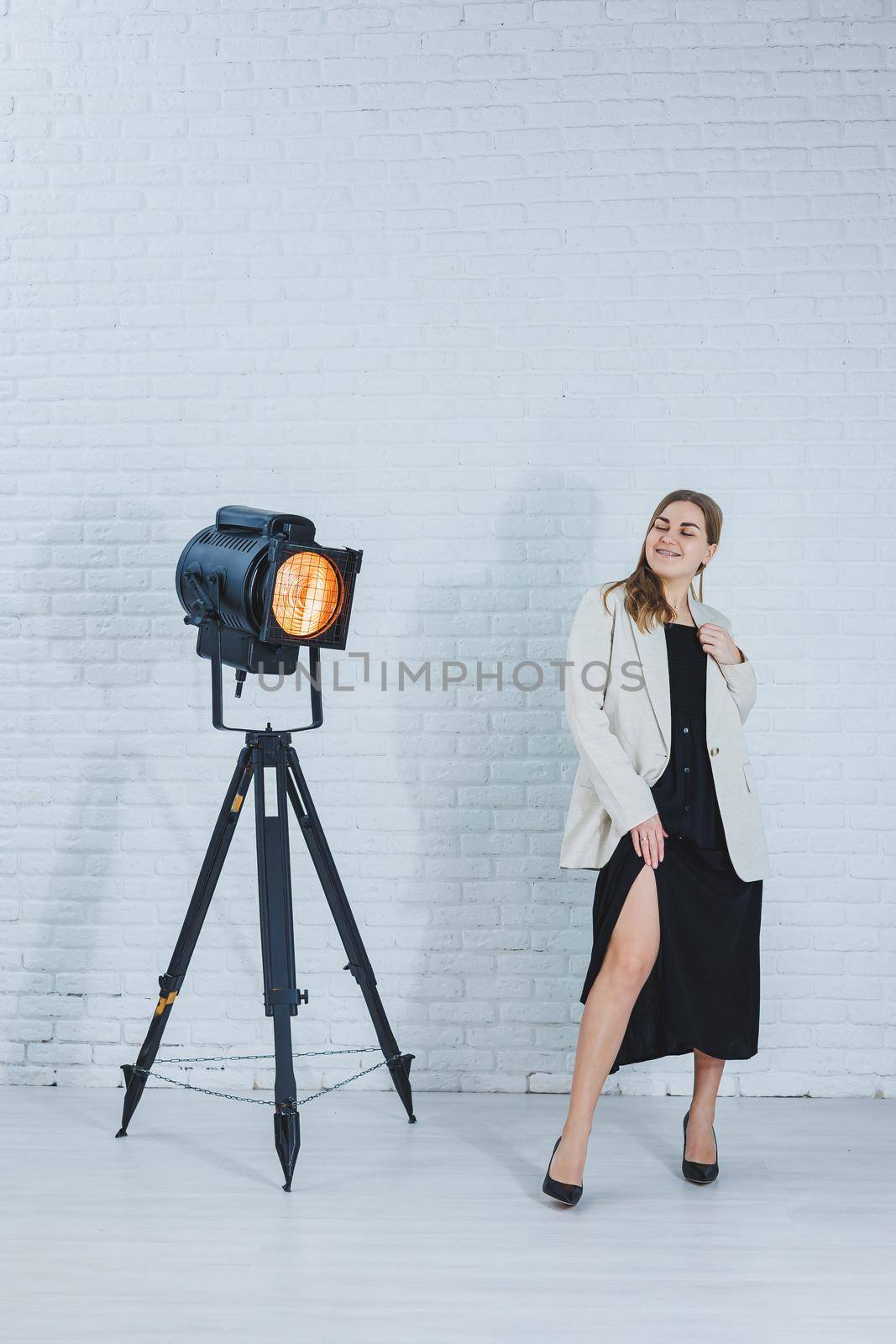 Gorgeous slender brown-haired woman in a black dress and a beige jacket, long bare legs and high heels. Black pumps on female feet by Dmitrytph