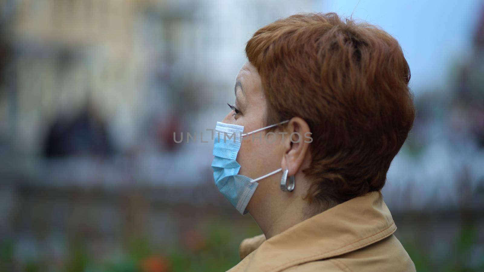 Side view of a woman's hands putting on a protective medical mask against coronavirus in a crowded place in the city. by Petrokill