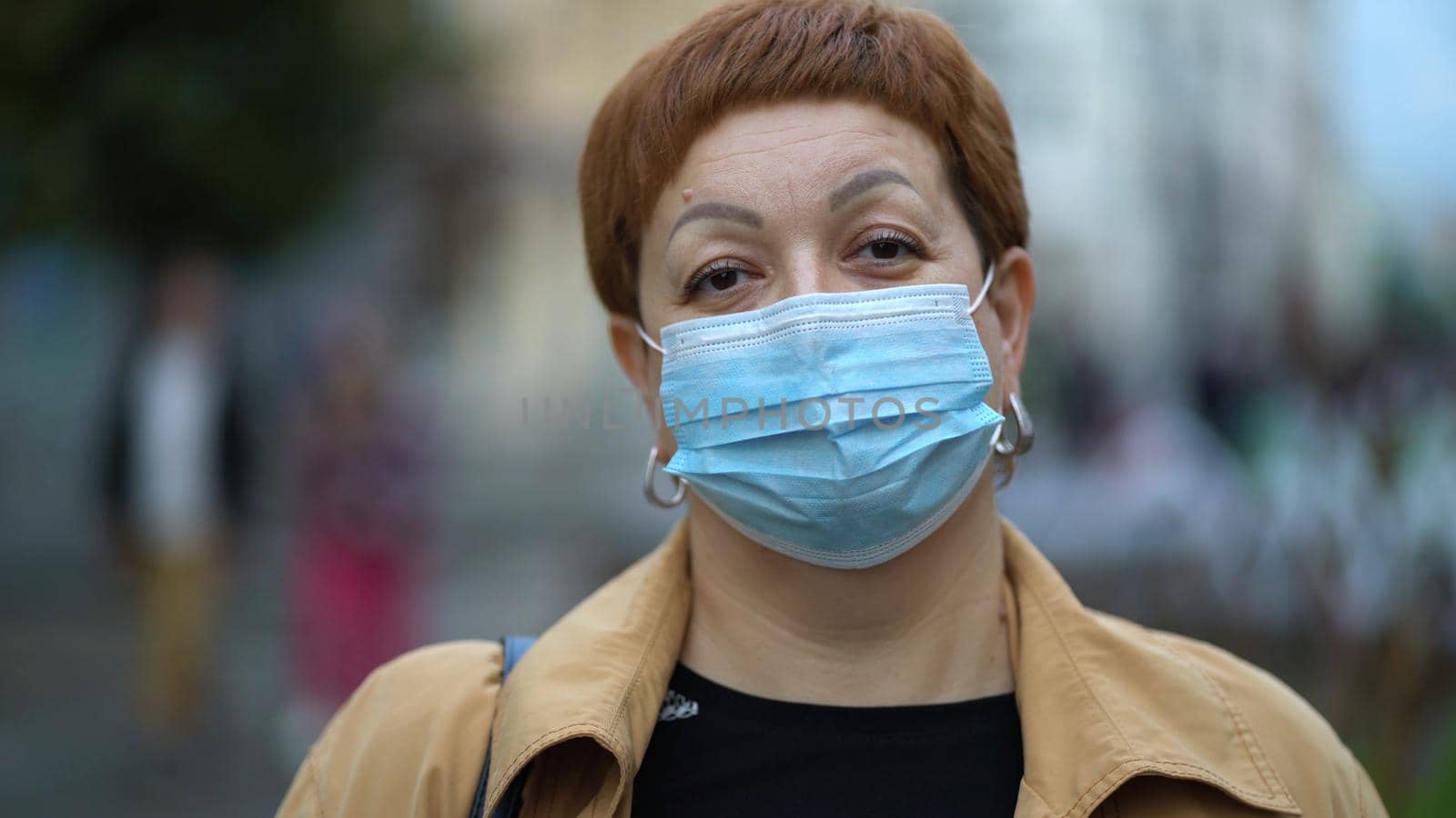 Sad red-haired middle-aged woman in wears a medical mask on the street to prevent the spread of the virus, coronavirus, infected by respiratory.