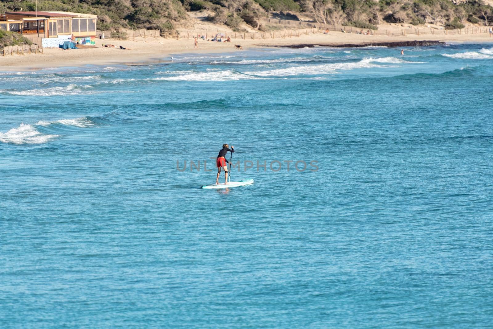 Man practicing paddle surfing through the deserted beaches of Ses Salines in the Ses Salinas National Park of Ibiza and Formentera, Spain.