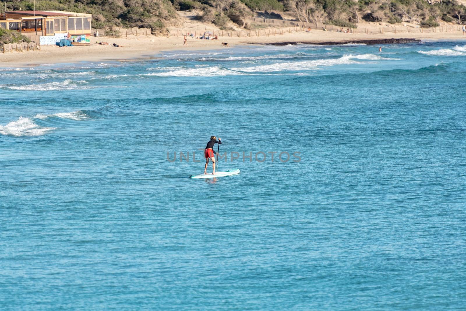 Man practicing paddle surfing through the deserted beaches of Ses Salines in the Ses Salinas National Park of Ibiza and Formentera, Spain.