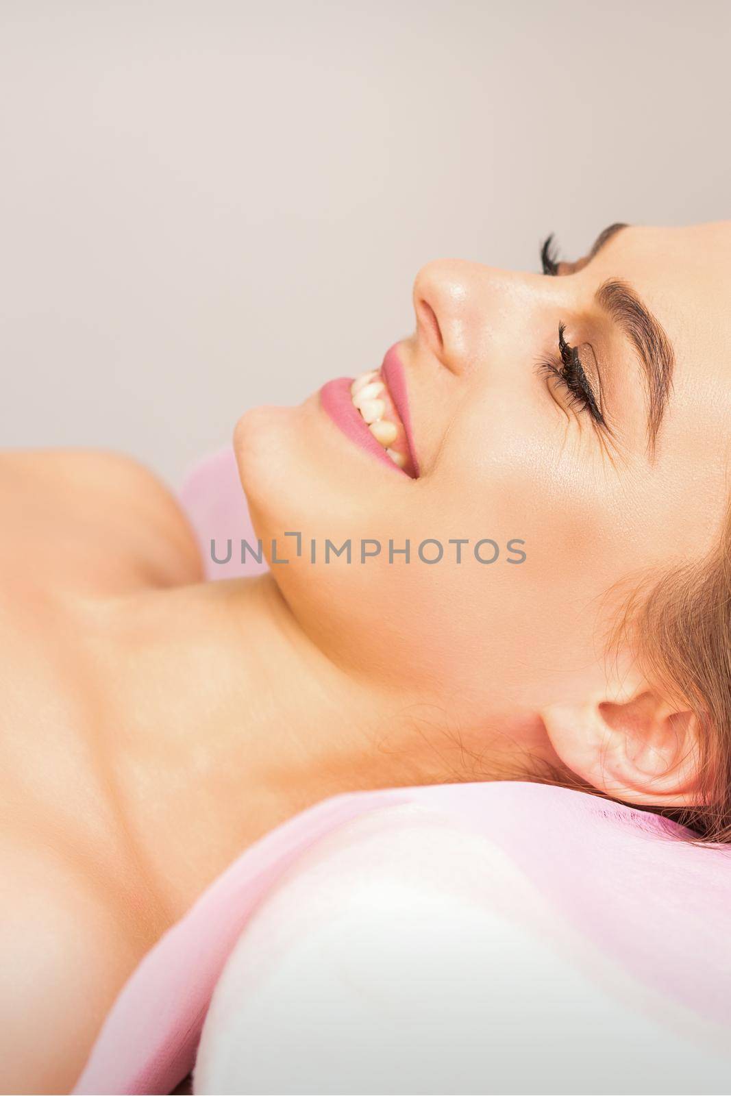 A beautiful smiling young woman is lying on a massage couch waiting for a massage in a massage room
