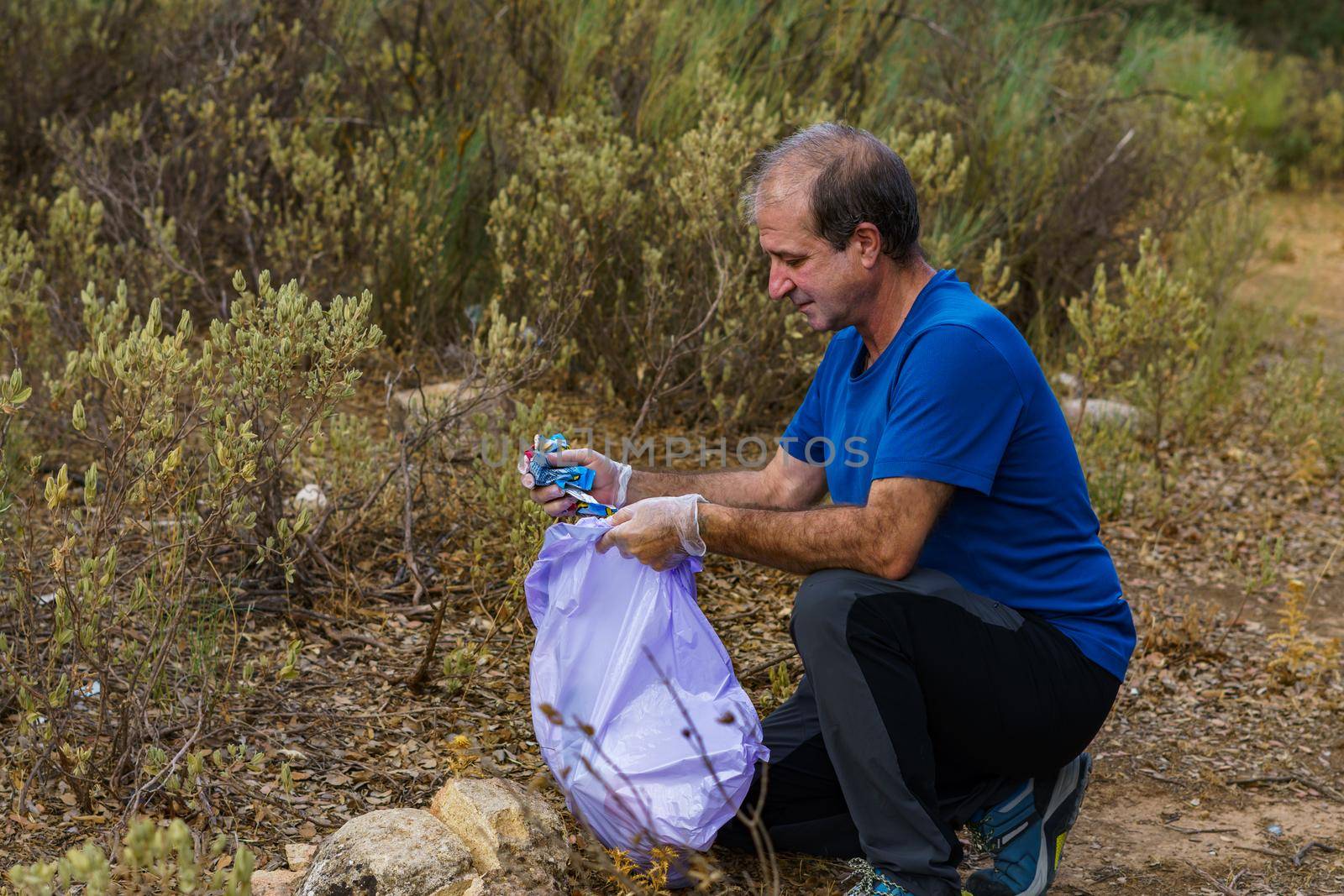 environmentalist man with garbage bags picking up garbage from the field and taking care of the environment