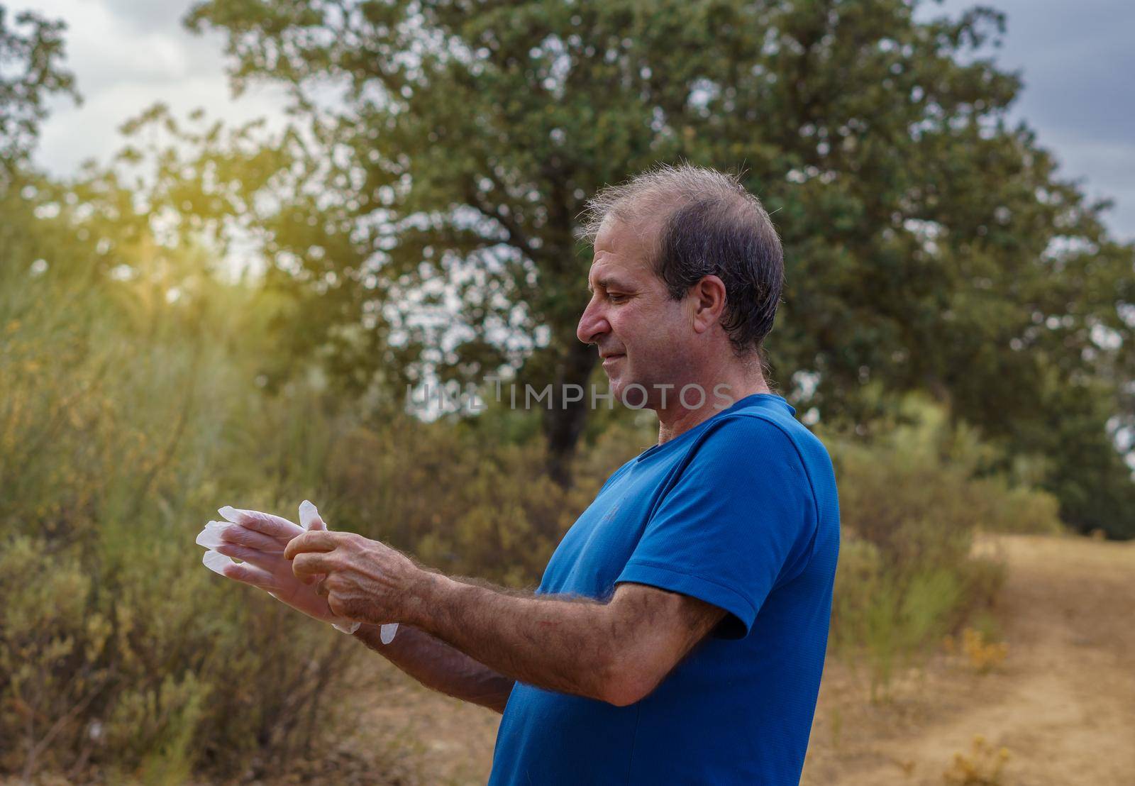 close-up of a male volunteer environmentalist putting on latex gloves to clean the bush with the sun in the background