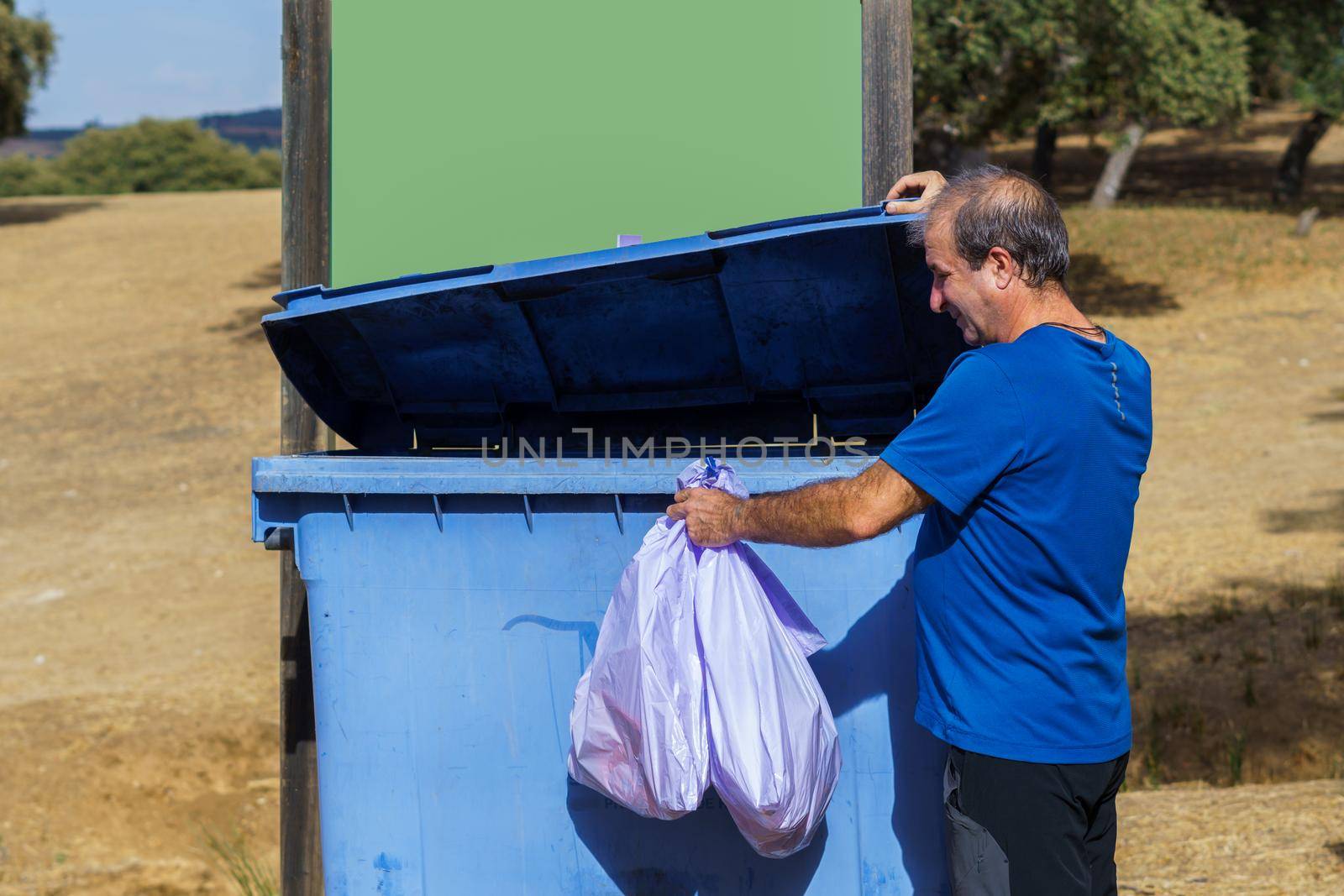 man throwing bags of garbage into a dumpster by joseantona