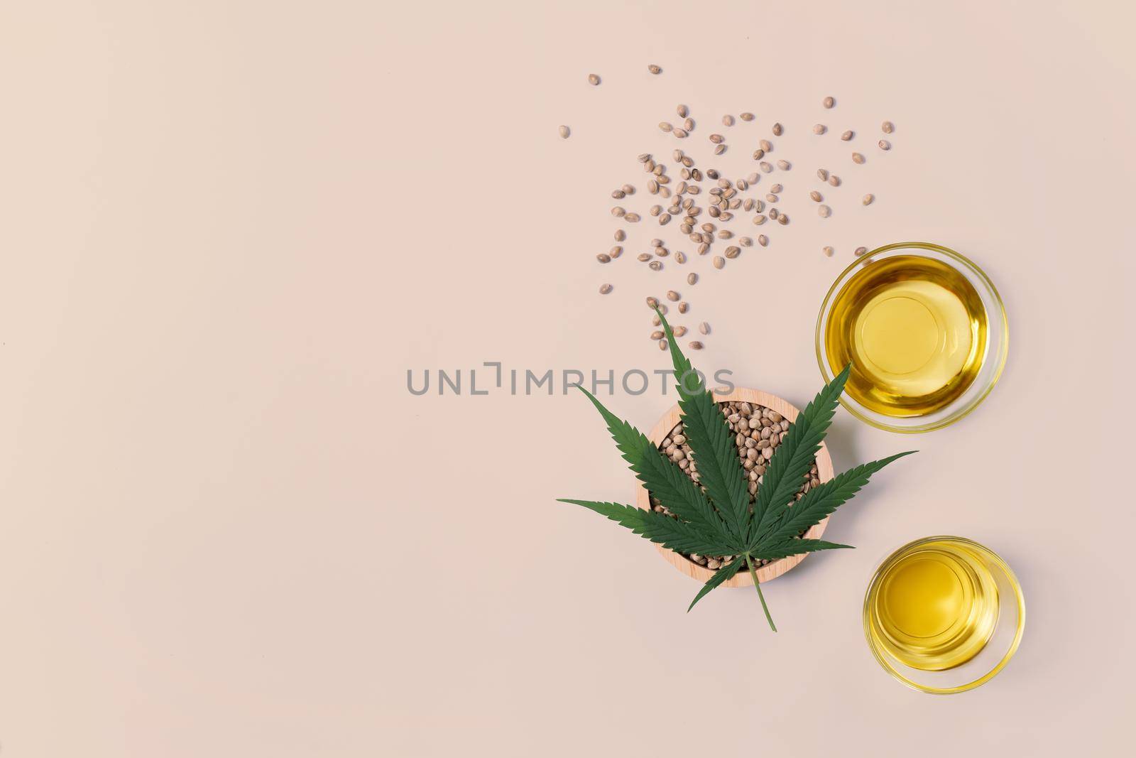 CBD oil, THC tinture in glass bowl and bottle with dropper lid and hemp leaf on empty background with a pile of dry hemp seeds surrounded in minimalism. Legalized marijuana concept.