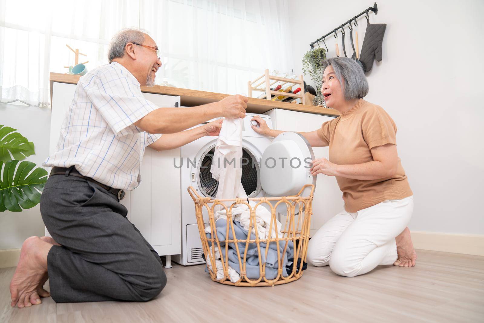 Senior couple working together to complete their household chores at the washing machine in a happy and contented manner. Husband and wife doing the usual tasks in the house.