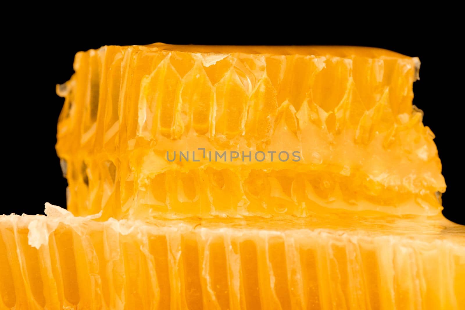 Close up stack of several fresh cut golden comb honey slices on plate isolated on black background, low angle, side view