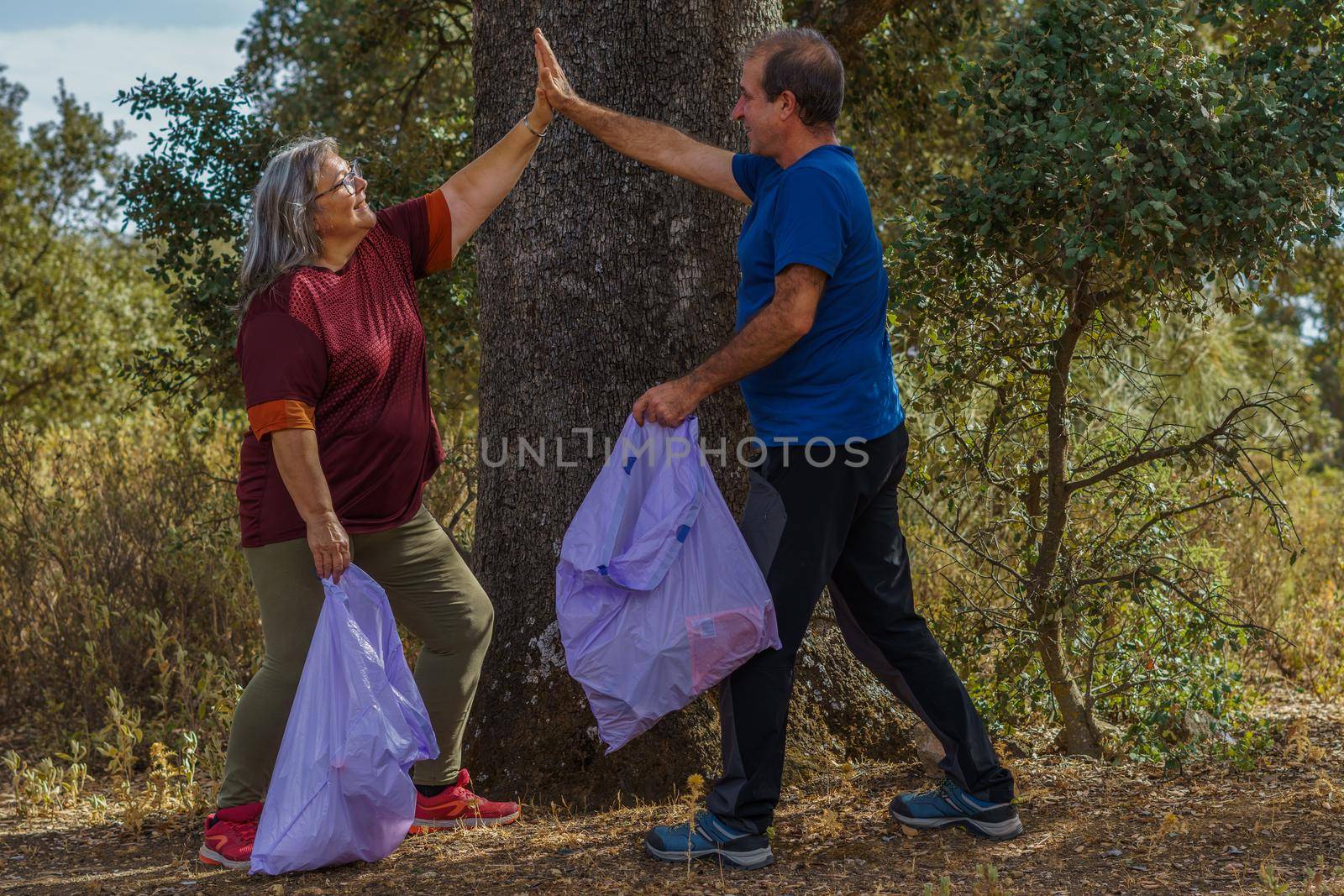 environmentalist couple high-fiving in the bush cleanup with garbage bags in their hands.