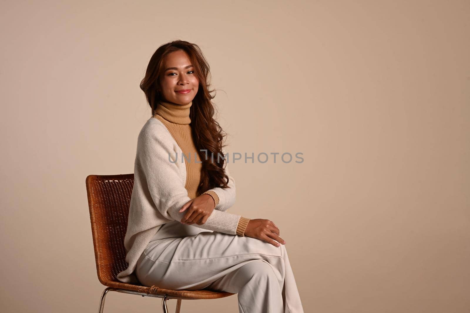 Attractive woman wearing stylish trendy clothes in earth tones sitting on beige background. Autumn and Winter concept.