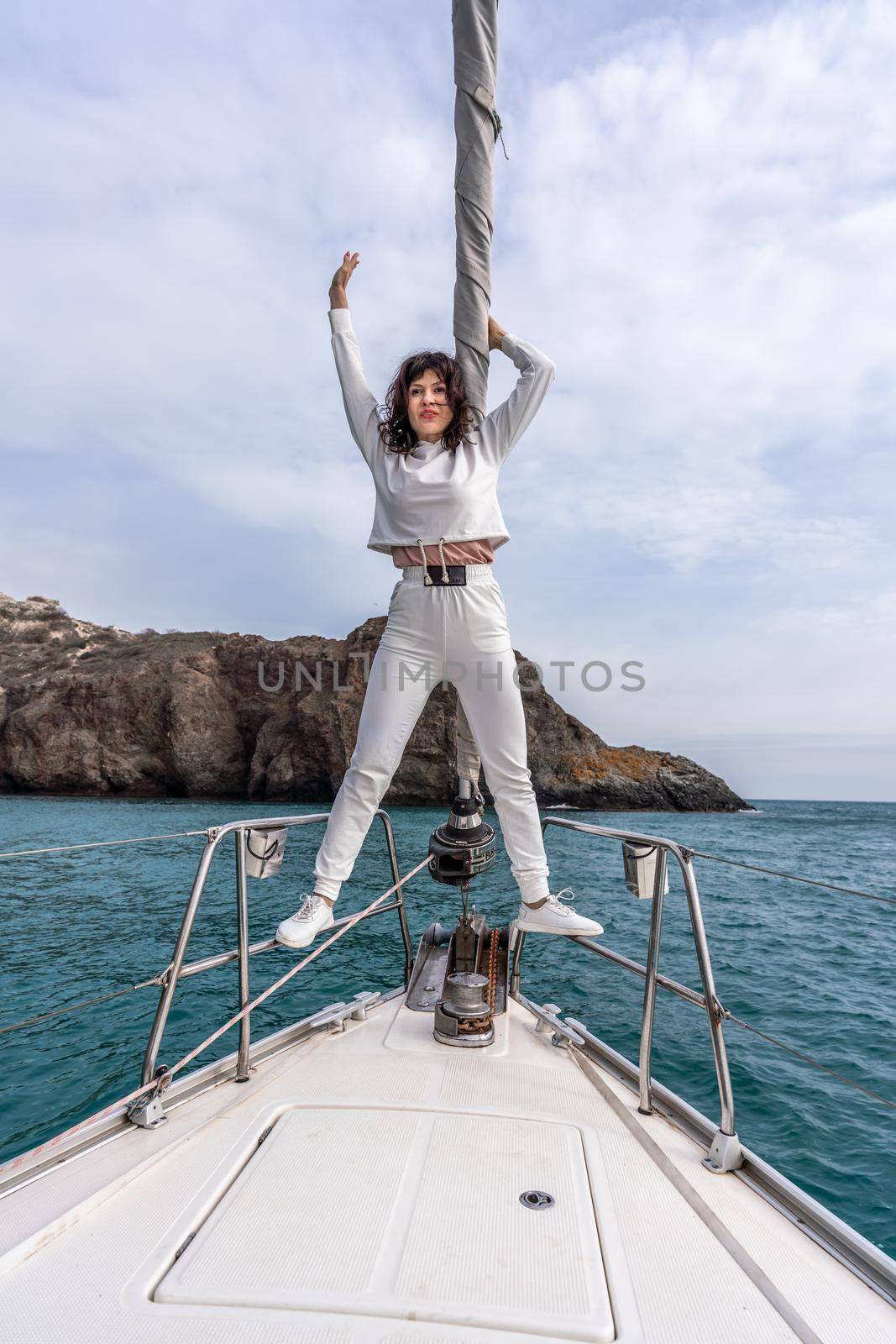 Woman standing on the nose of the yacht at a sunny summer day, breeze developing hair, beautiful sea on background.