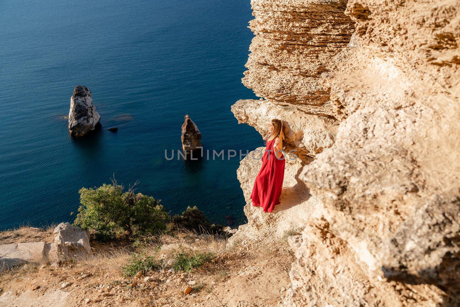 A woman in a red flying dress fluttering in the wind, against the backdrop of the sea