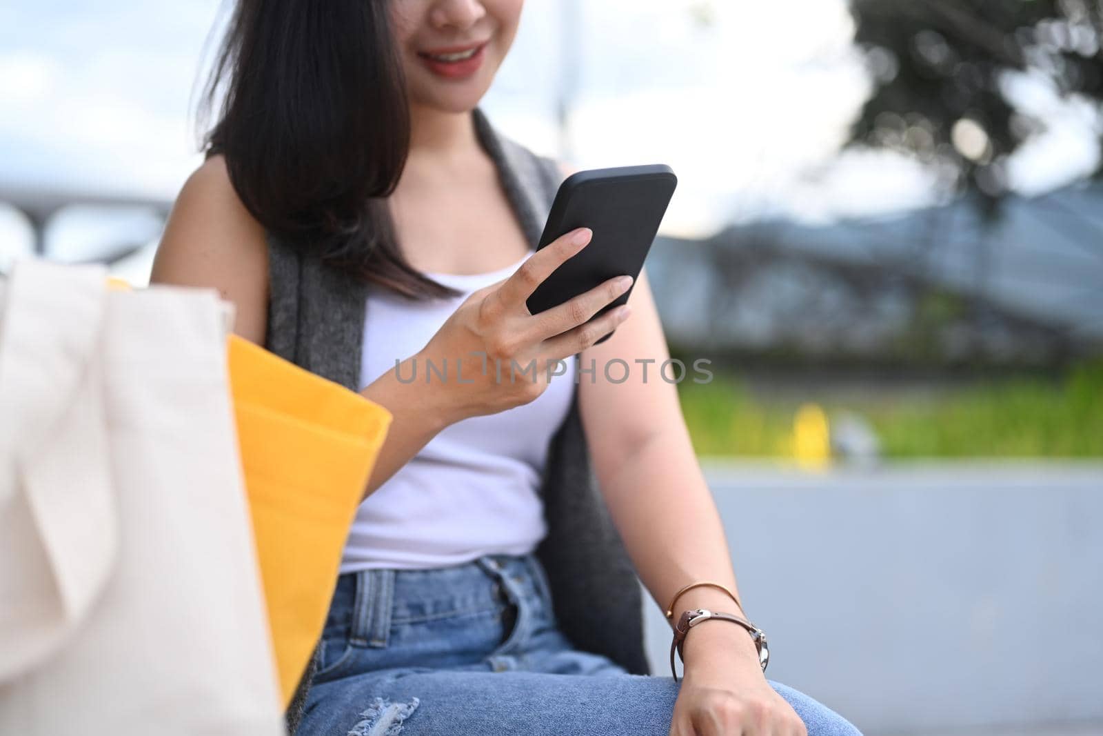 Young woman sitting on bench in the park and communication in social networks via smart phone.