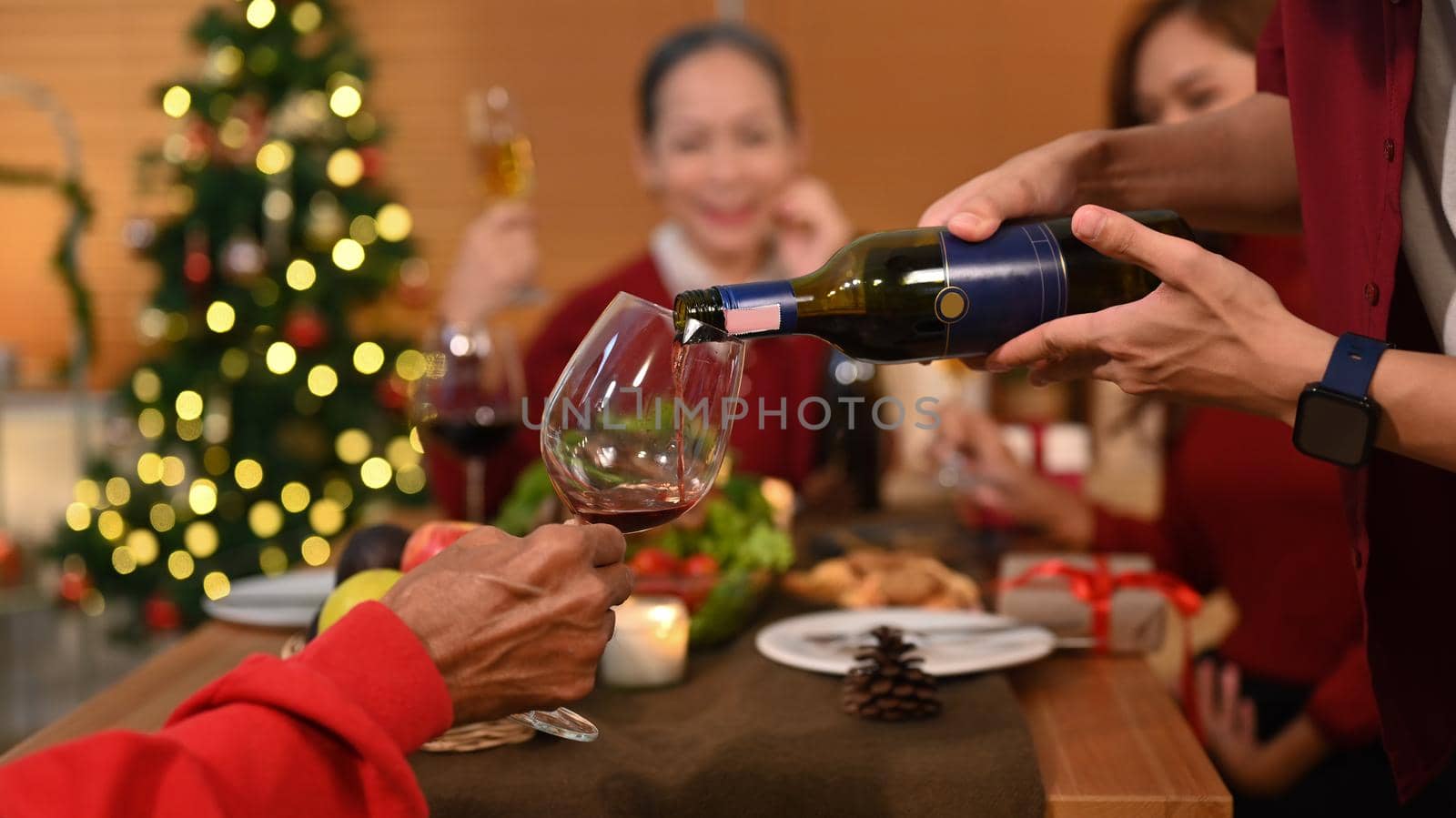Man pouring wine to his grandparent while having Christmas dinner. Celebration, holidays and party concept by prathanchorruangsak