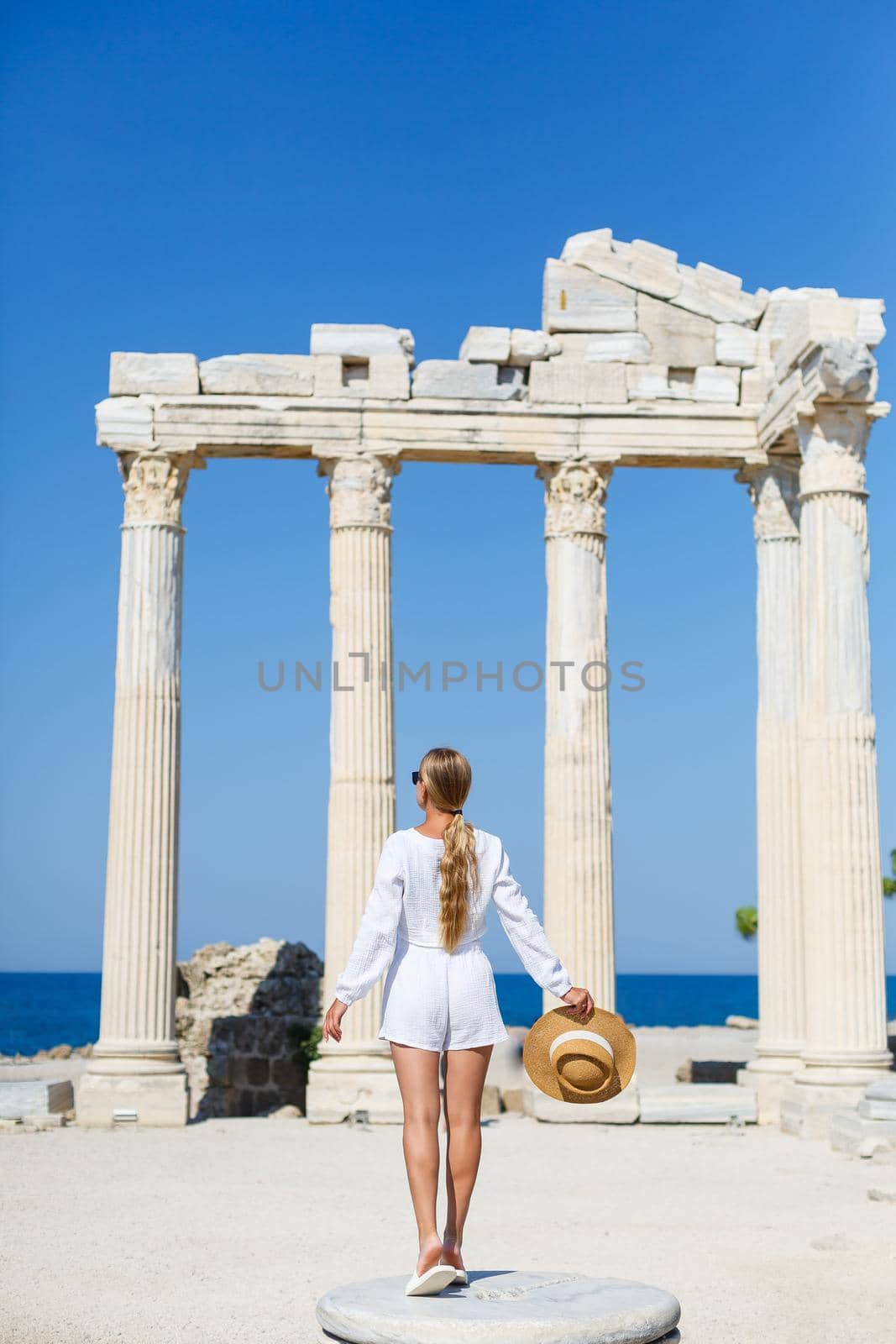 A young slender tanned woman in white shorts and a T-shirt, wearing sunglasses and a hat. Walk on a hot sunny day