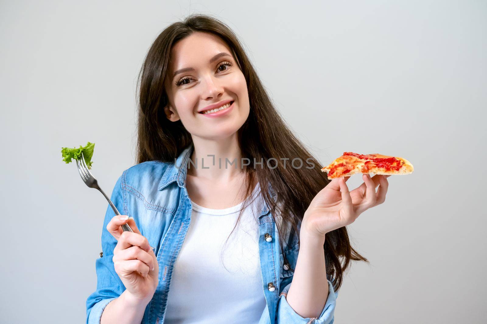 Young smiling woman chooses what to eat, pizza or salad.