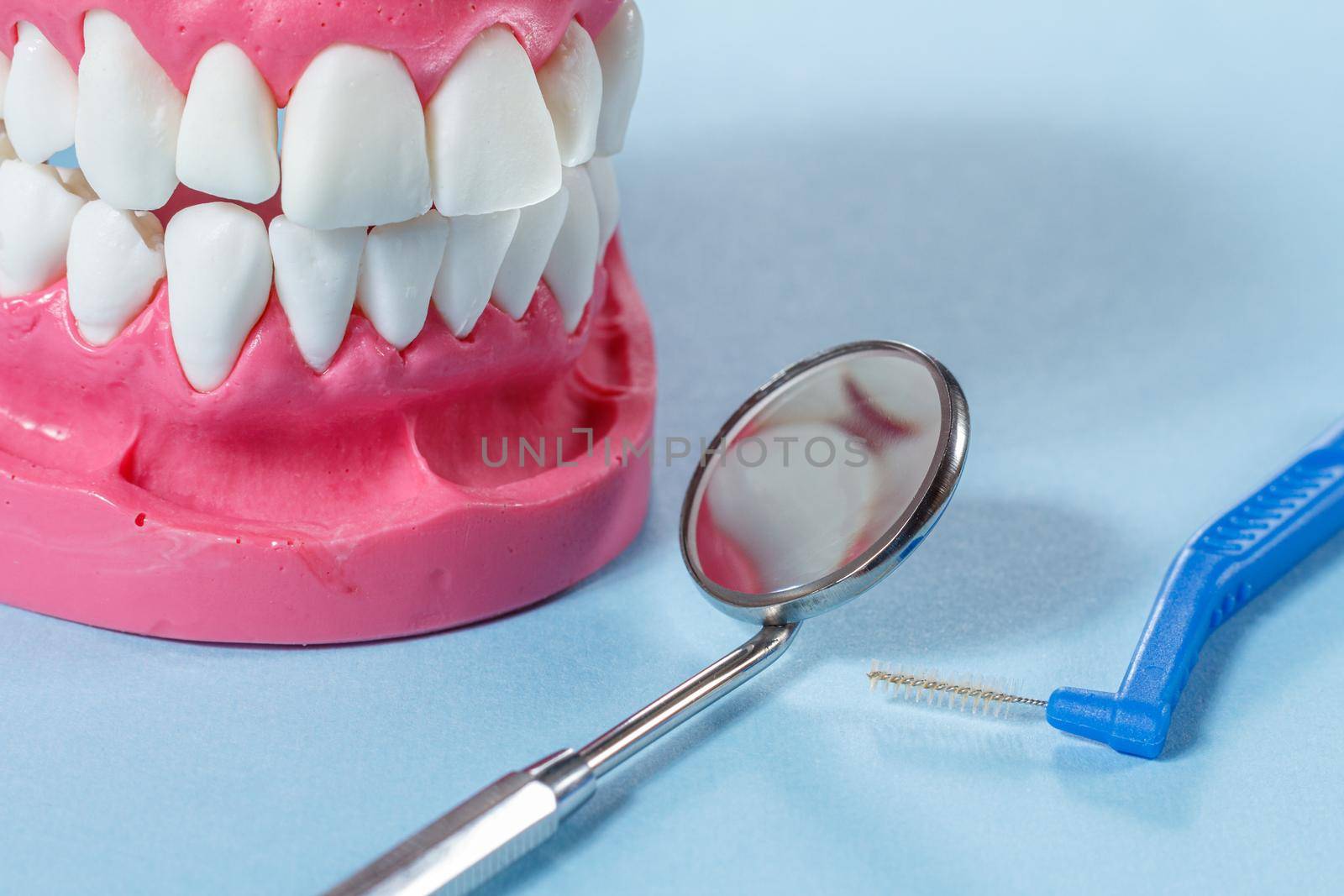 Close-up view of a metal mirror, a interdental brush and a human jaw layout on the background.