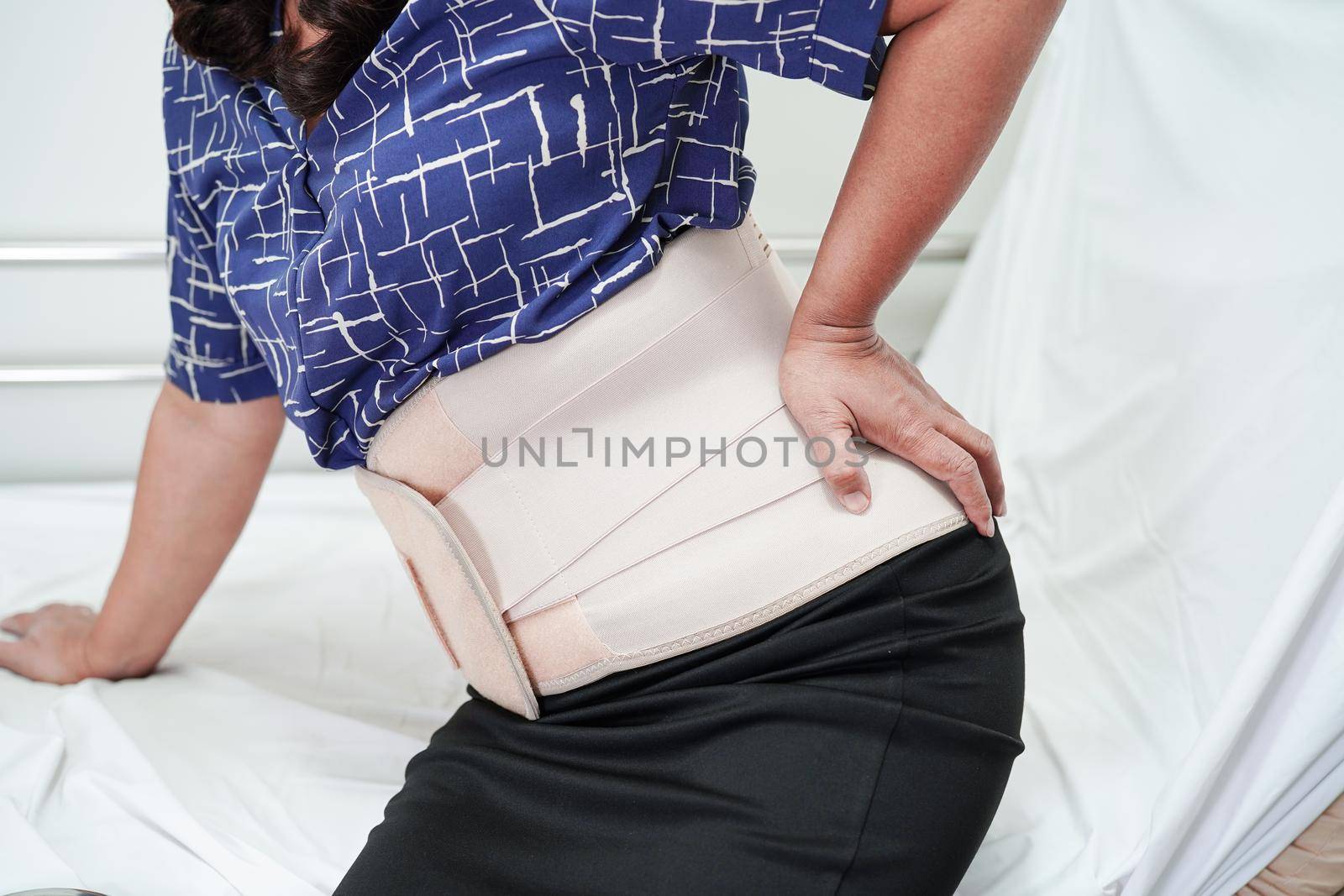 Asian senior wearing elastic support belt can help reduce back pain.