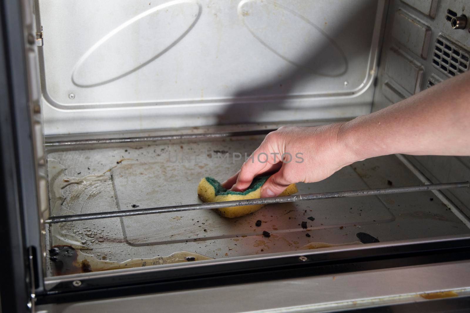 Female hand with sponge and detergent cleaning the kitchen oven from burnt drops, housekeeping concept. Scrubbing the stove, High quality photo