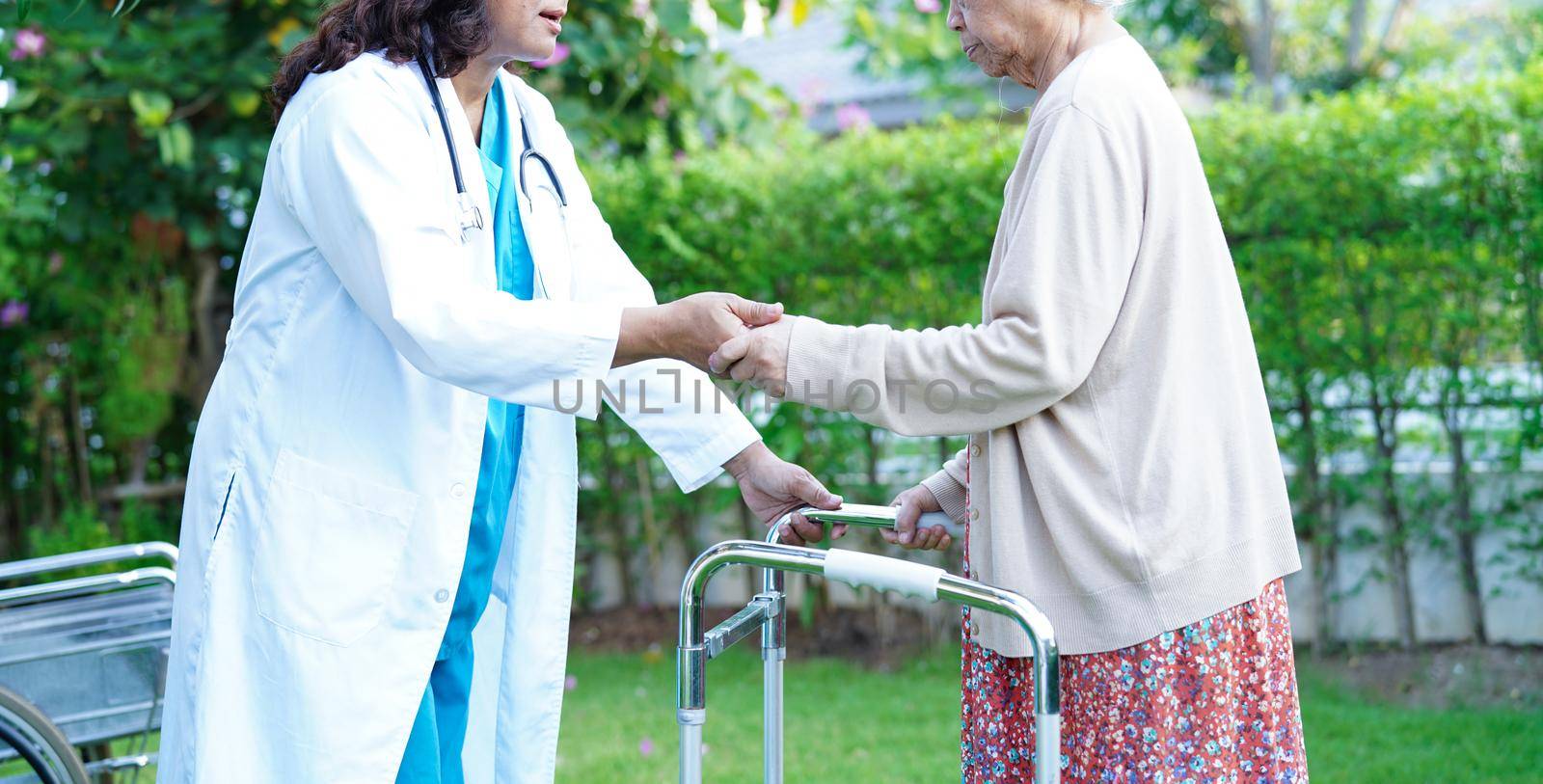 Doctor help Asian elderly woman disability patient walk with walker in park, medical concept.