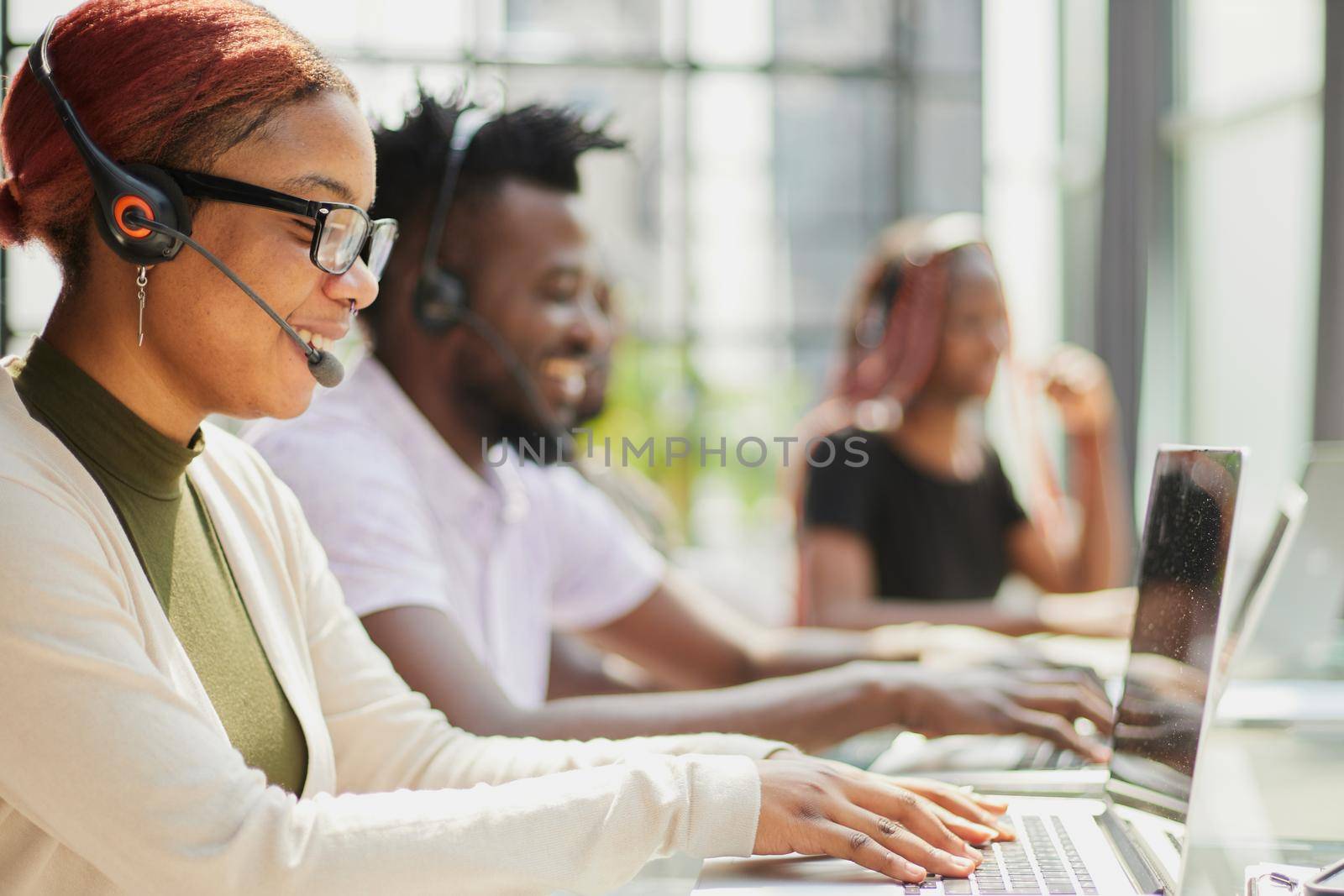 Smiling beautiful African American woman working in call center with diverse team by Prosto