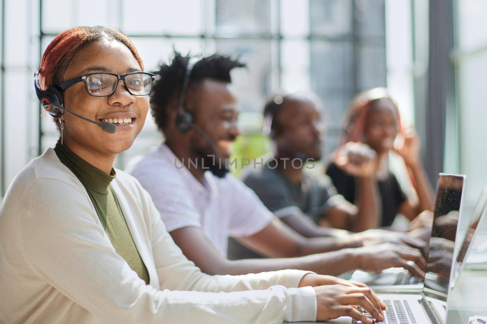 Smiling beautiful African American woman working in call center with diverse team by Prosto
