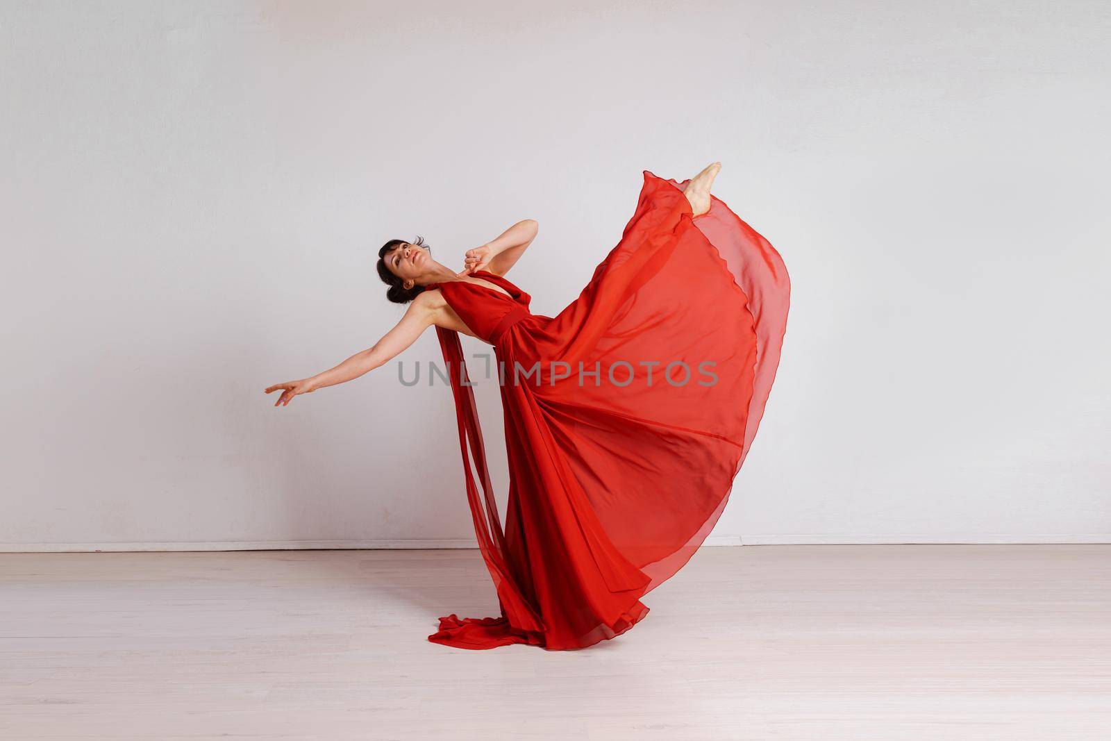 Dancer in a red flying dress. Woman ballerina dancing on a white studio background.