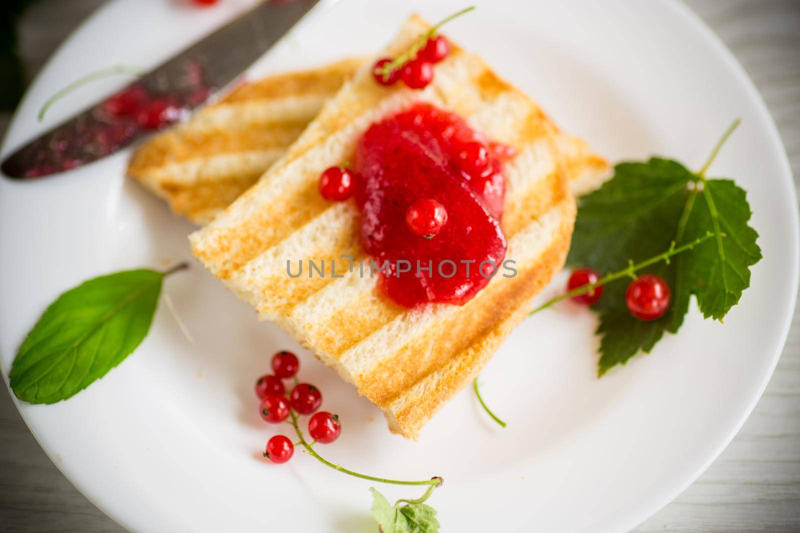 fried bread croutons for breakfast with redcurrant jam in a plate with berries on a wooden table.