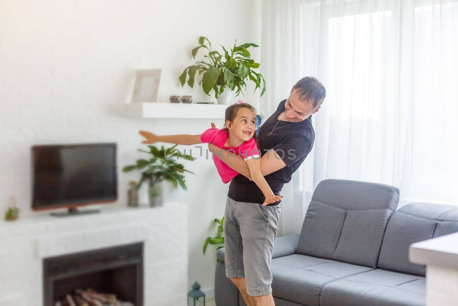 Nice and beautiful picture of father and daughter spending time together. she is flying. Her dad is doing the same thing. Both of them are happy.