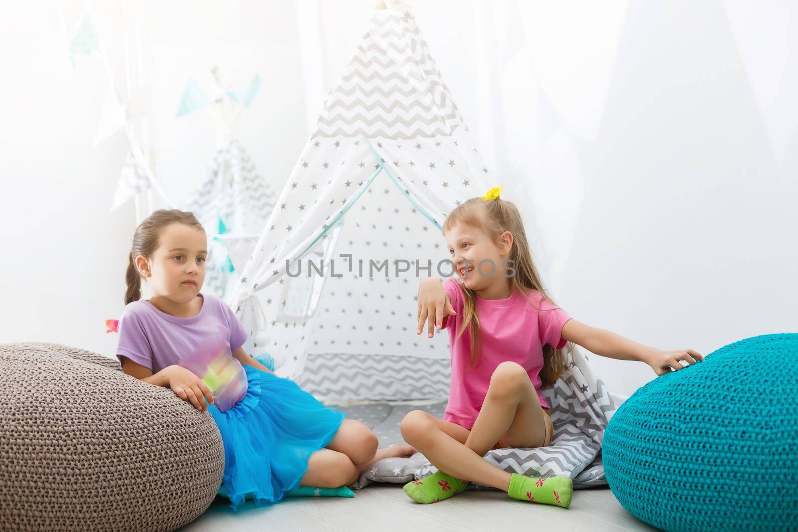 Two happy little girls are smiling while playing in children's room at home