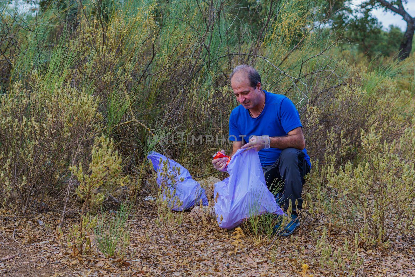 environmentalist man with garbage bags picking up garbage from the field and taking care of the environment