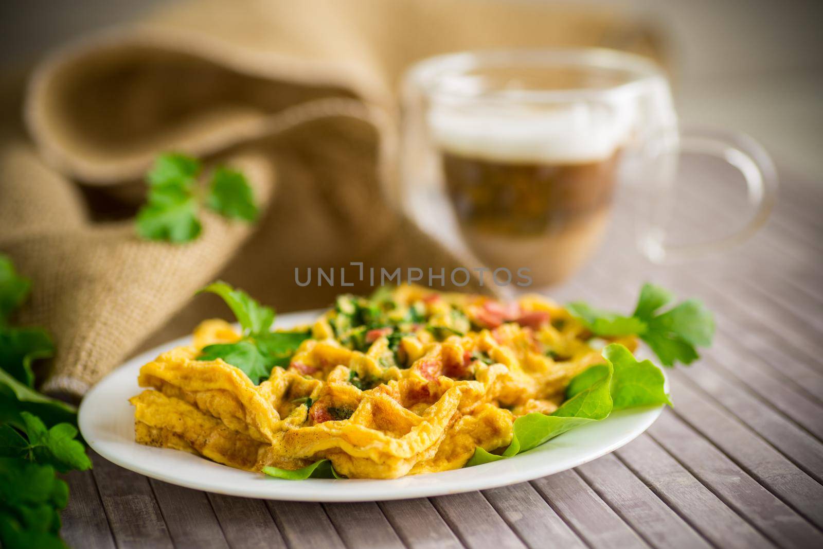 Egg omelet stuffed with greens and sausage fried in the form of waffles, on a wooden table