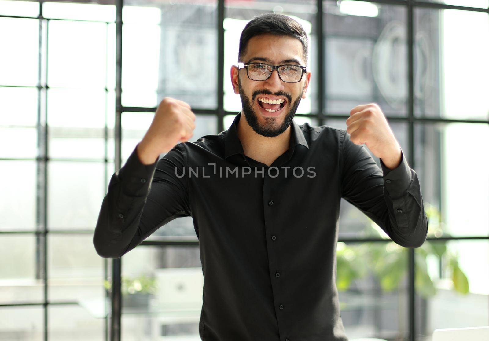 young businessman celebrating success in his home office holding fists up celebrating achievement