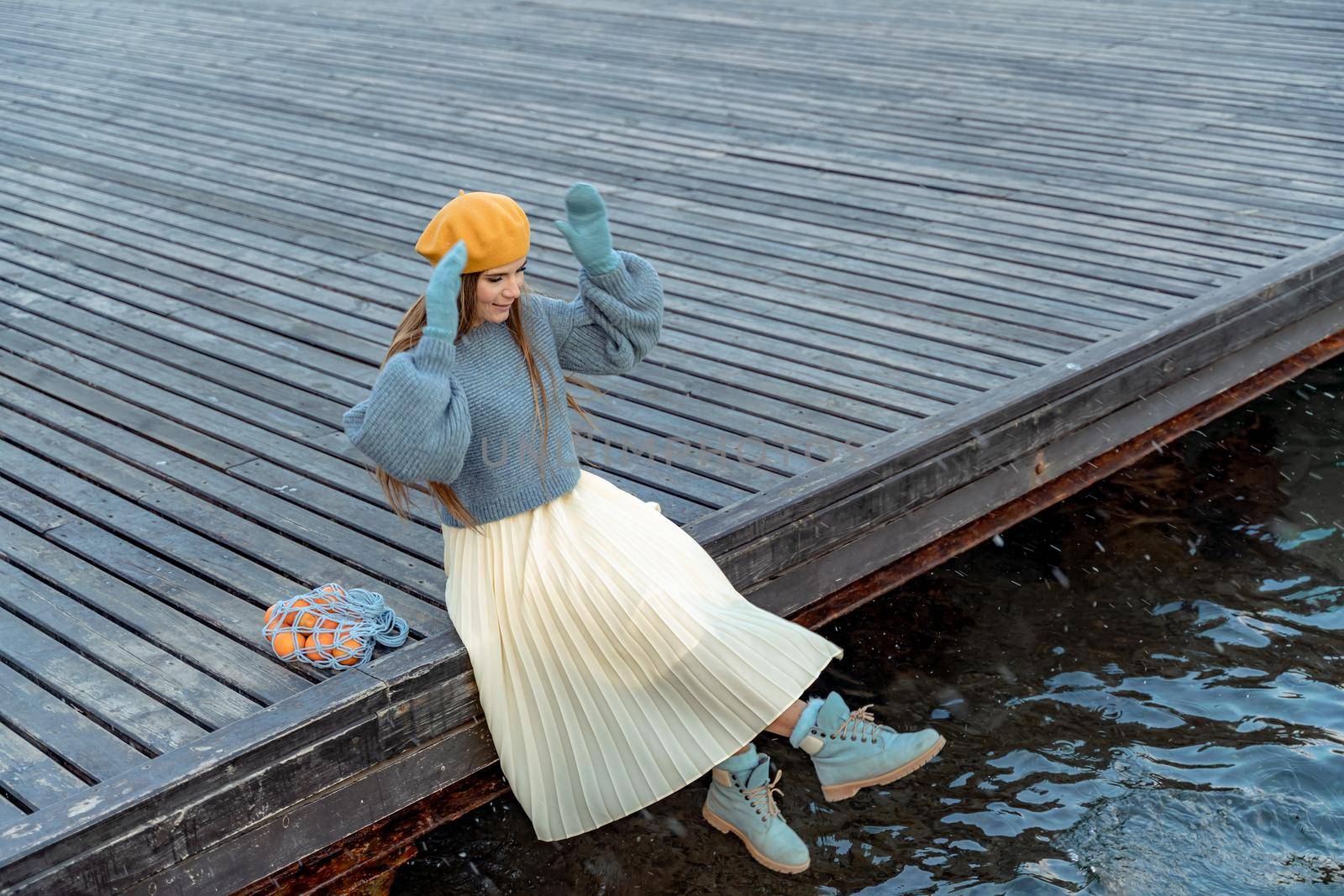 Outdoors fashion portrait of a beautiful middle aged woman walking on the beach. Marine background. Dressed in a stylish warm blue sweater, yellow skirt and beret. by Matiunina