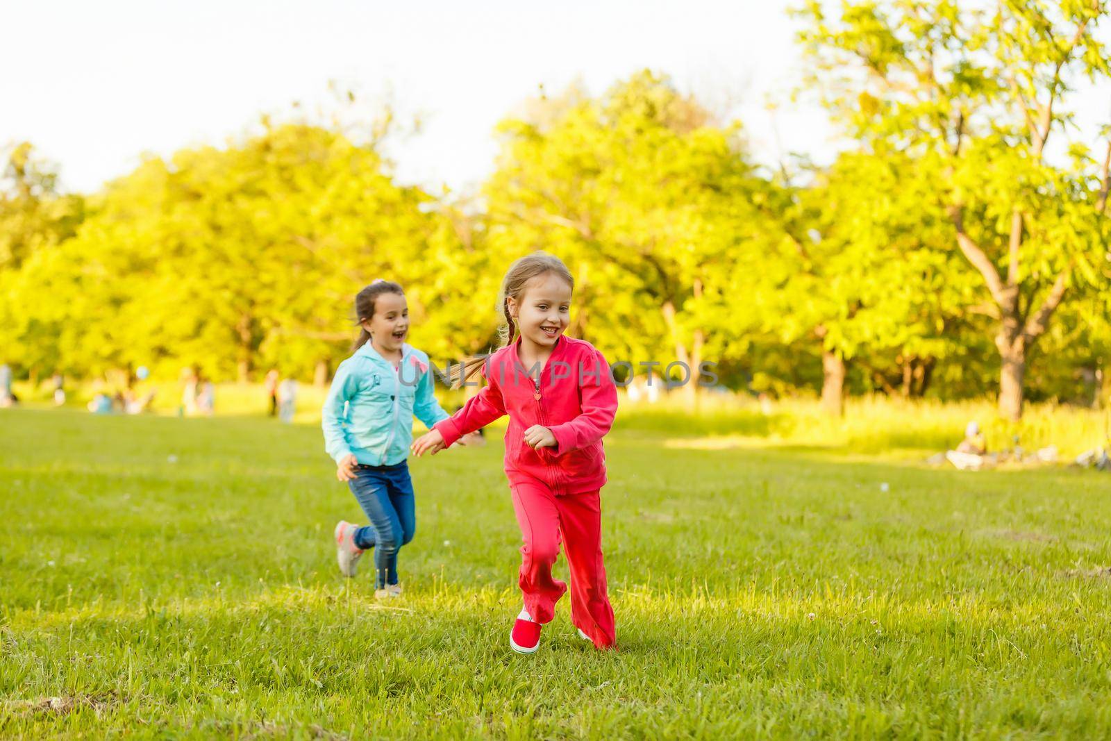 Children run on the green grass holding hands. Girls running around the lawn with grass playing with splashes of water to water plants.