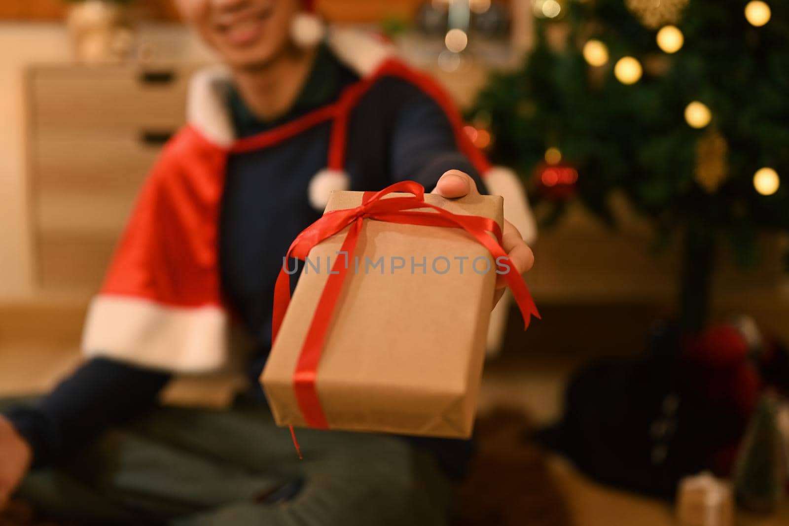 Close up view man hand holding Christmas gifts and sitting in decorated room lighted with soft lights.