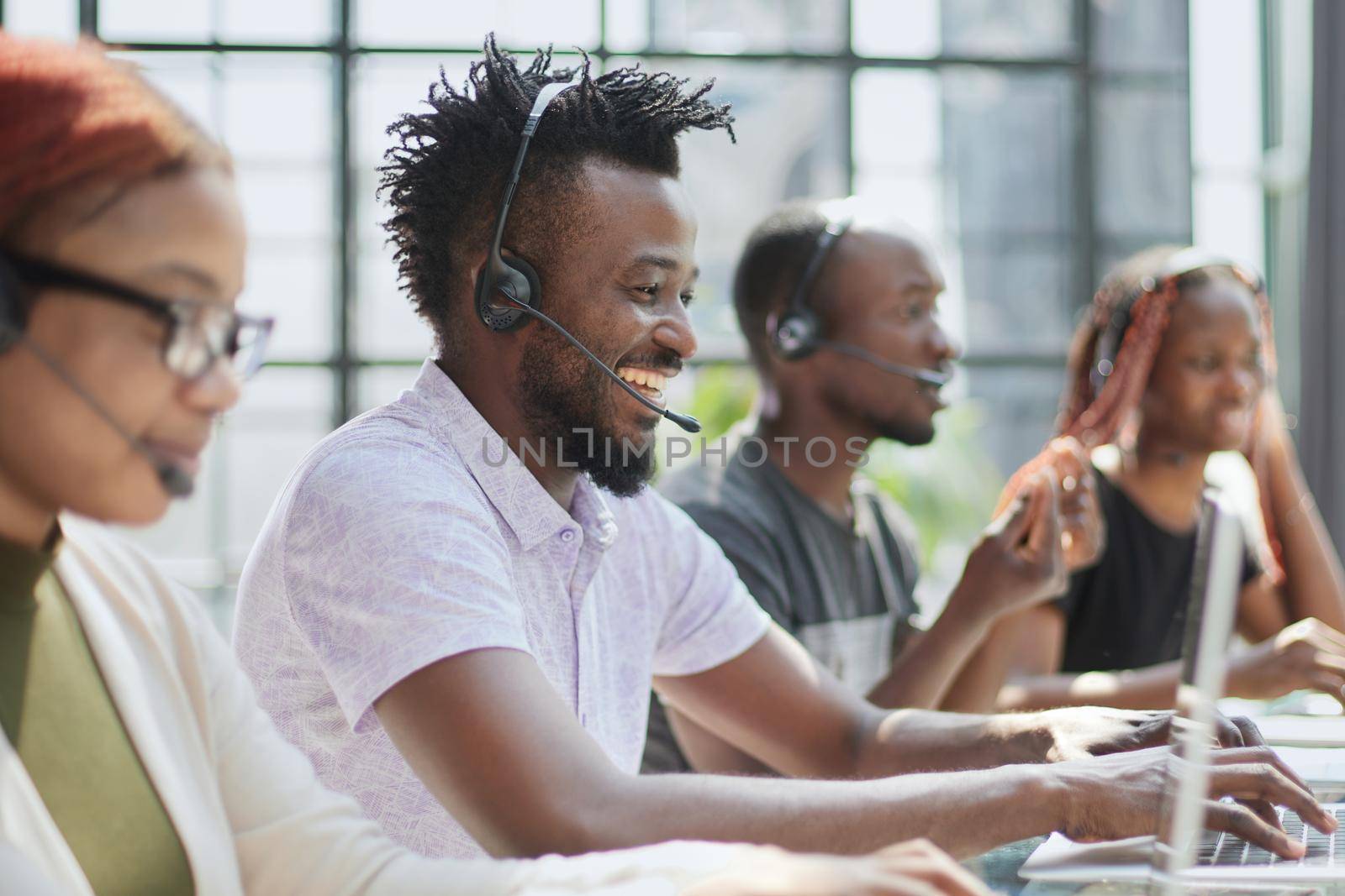 Smiling beautiful African American woman working in call center with diverse team by Prosto