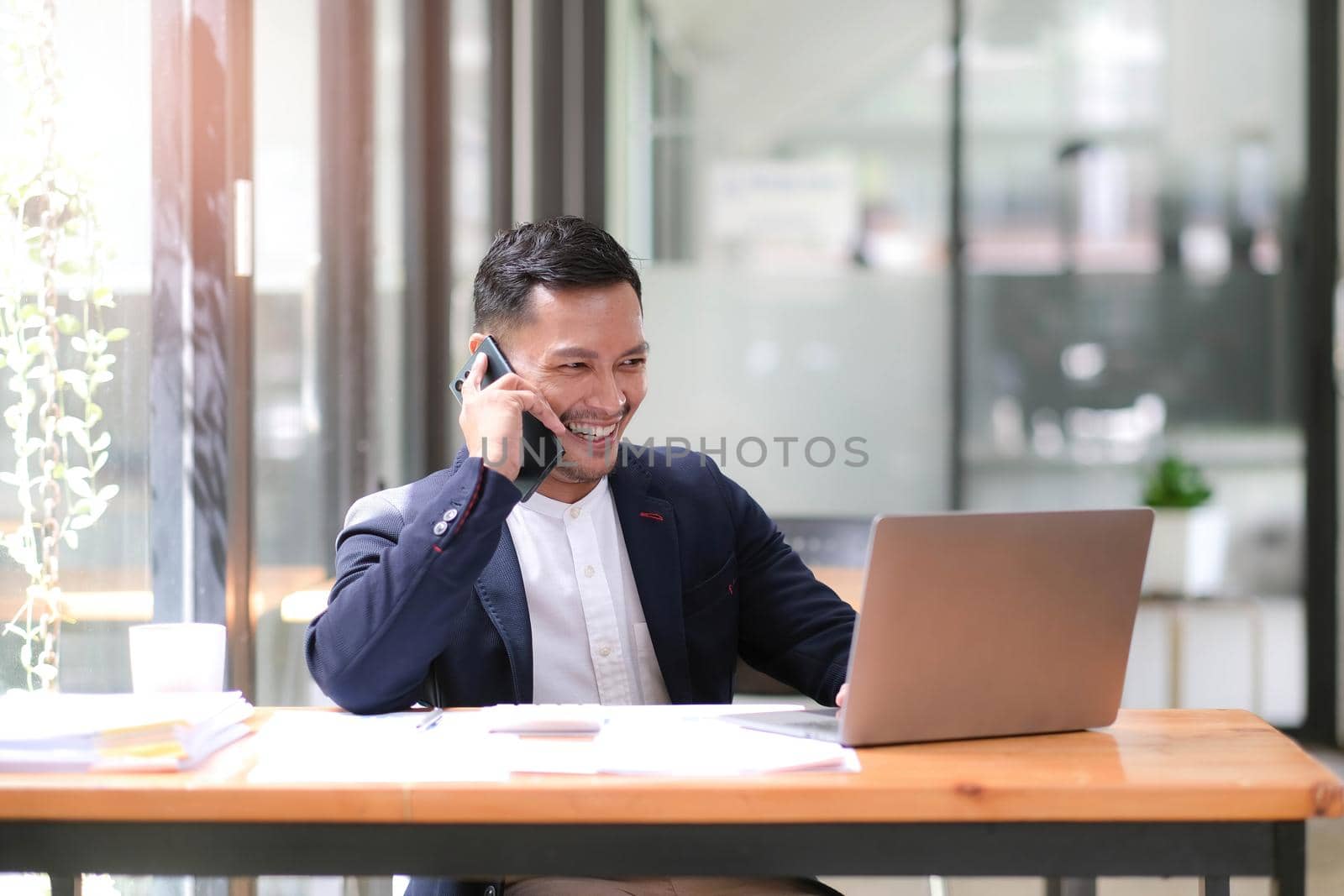 Asian businessman sitting on the phone with a customer with a laptop and document at his office desk..