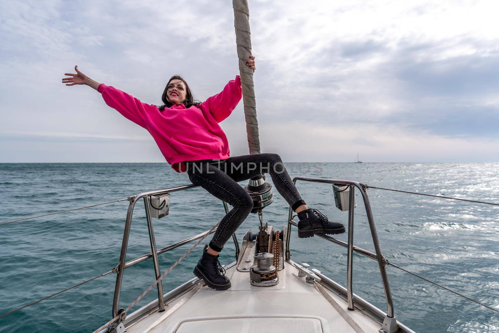 Woman standing on the nose of the yacht at a sunny summer day, breeze developing hair, beautiful sea on background.