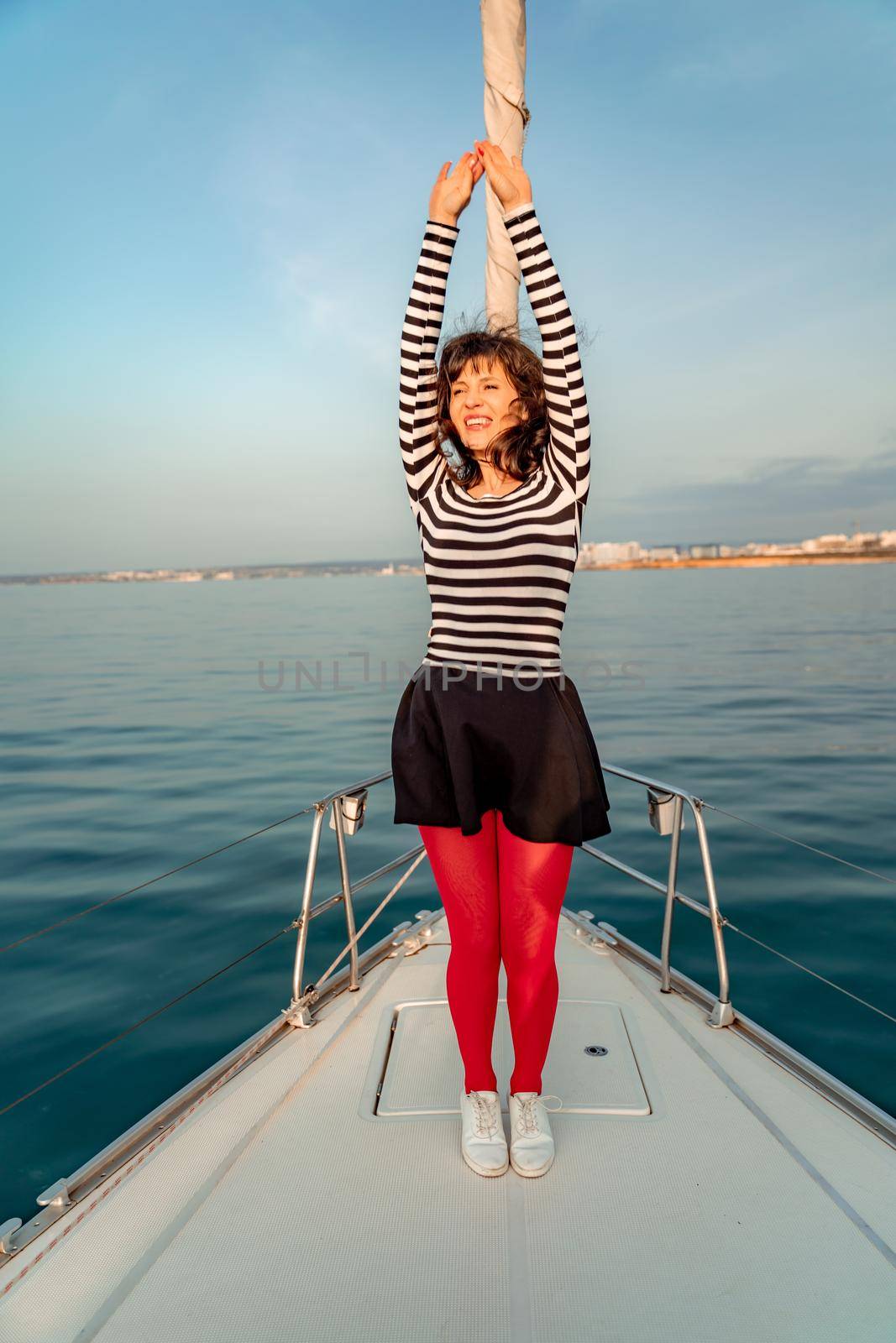 Woman standing on the nose of the yacht at a sunny summer day, breeze developing hair, beautiful sea on background by Matiunina