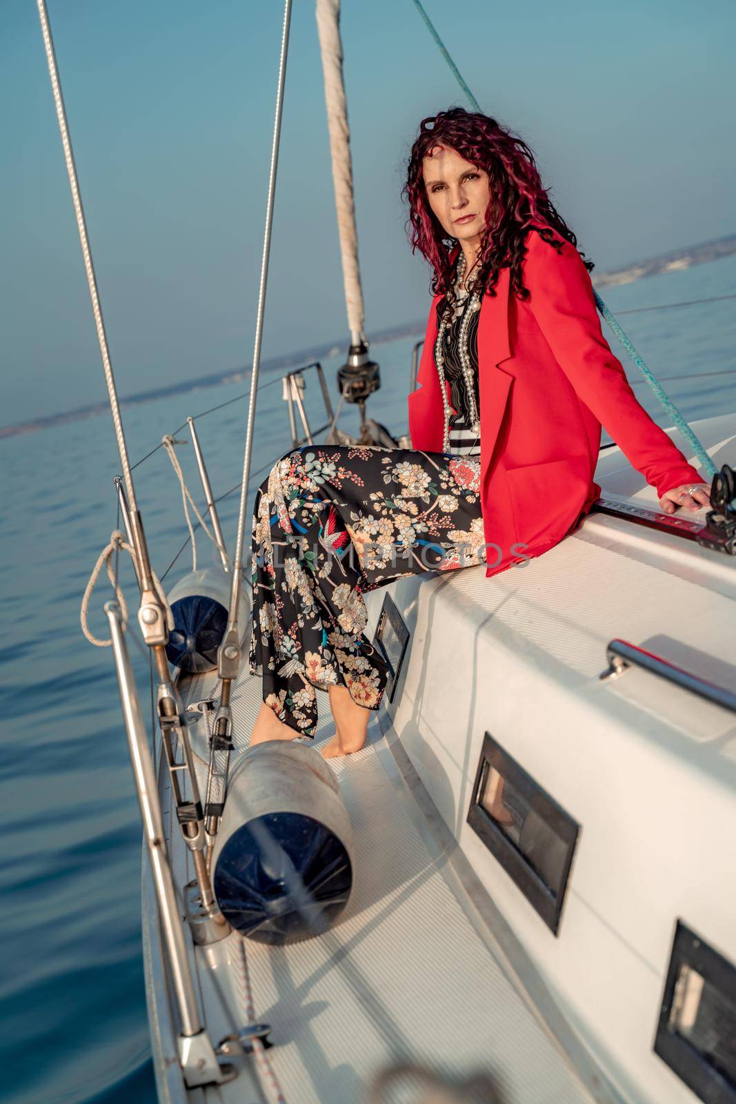 A woman sits on the bow of a yacht on a sunny summer day, the breeze develops her hair, a beautiful sea is in the background.