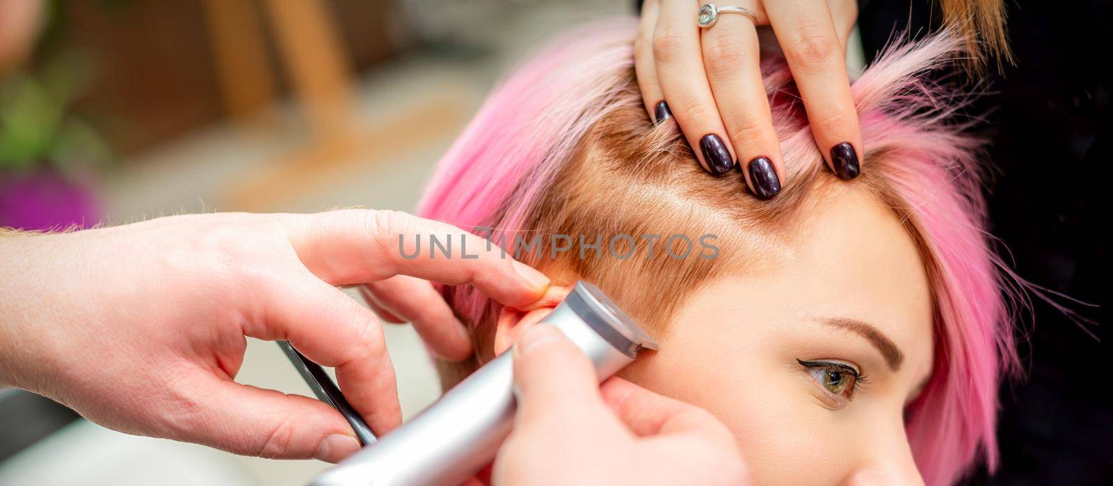 Hairdresser shaves female temple with pink hair by electric shaver in a hairdresser salon, close up