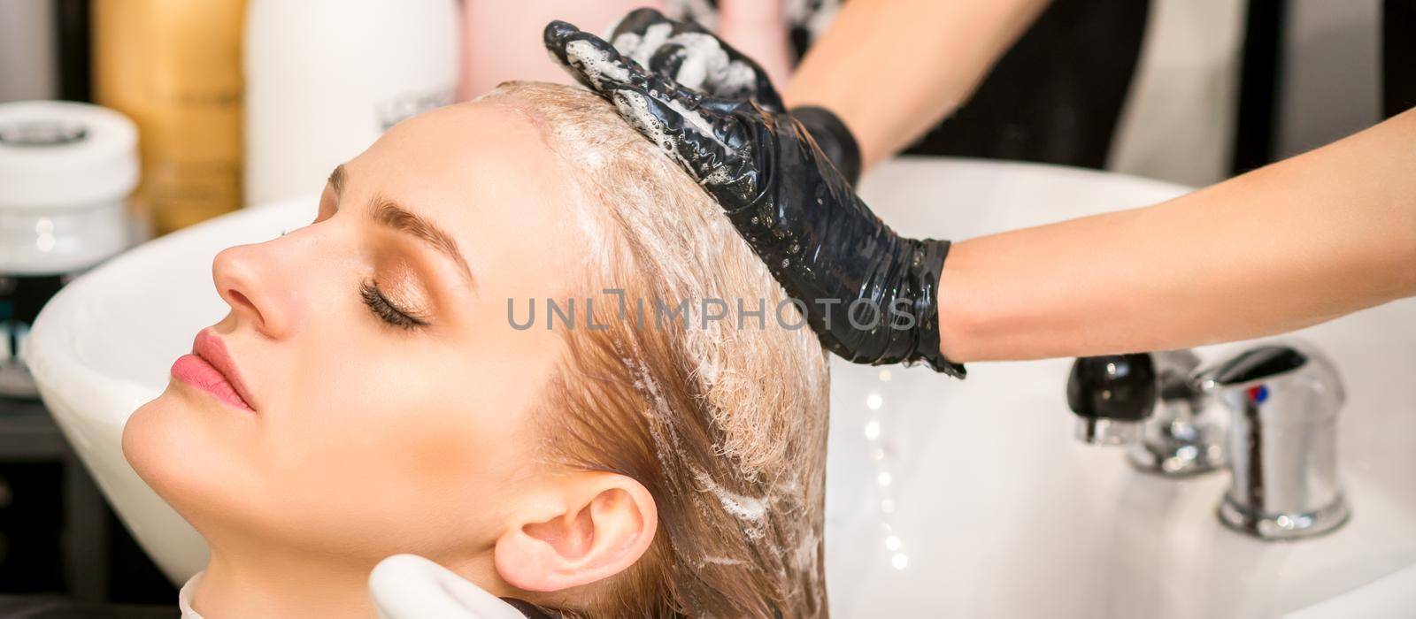 Young caucasian woman with closed eyes getting washing hair by a professional hairdresser in a beauty hair salon. by okskukuruza