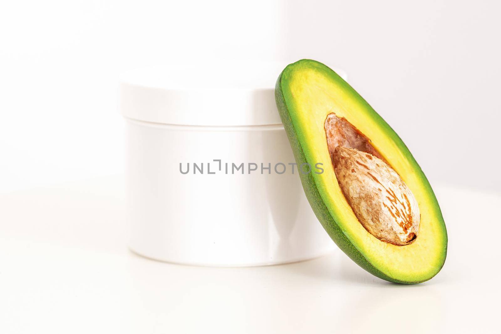 Skincare with natural cosmetics. White cosmetic jar of cream with half of the avocado near against white background, copy space, mockup. by okskukuruza