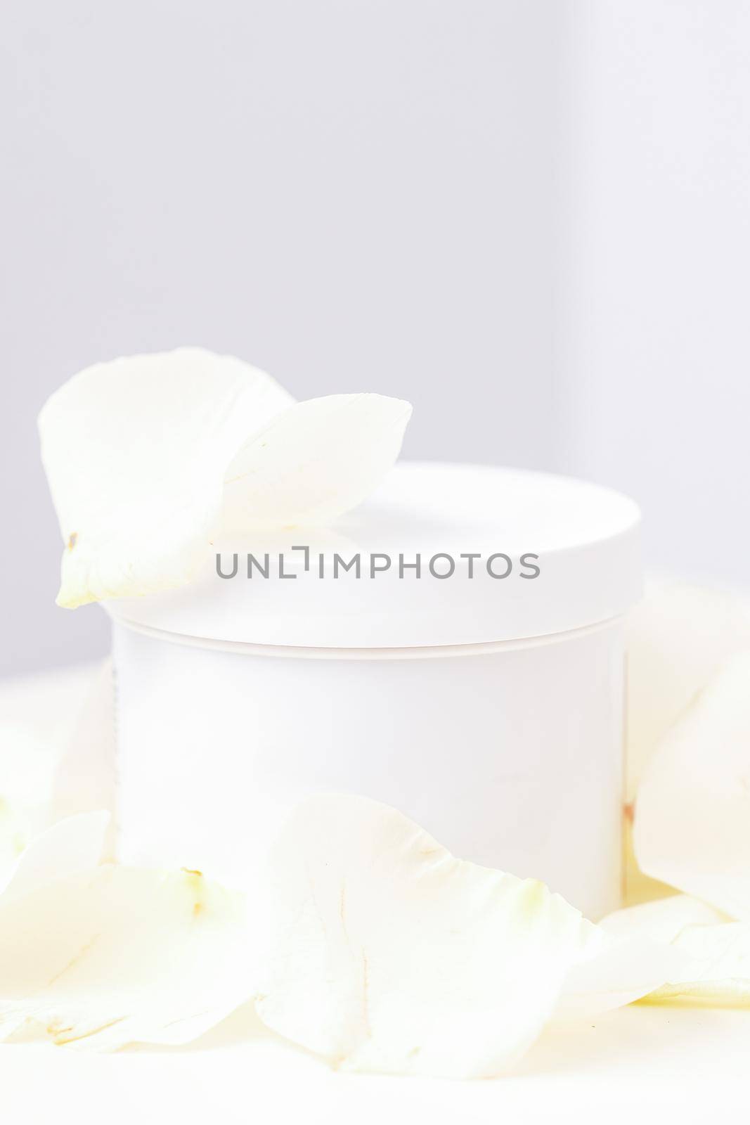 White jar with cream among delicate white rose flowers petals on a light background. Natural organic cosmetics concept, close up, mock-up. by okskukuruza