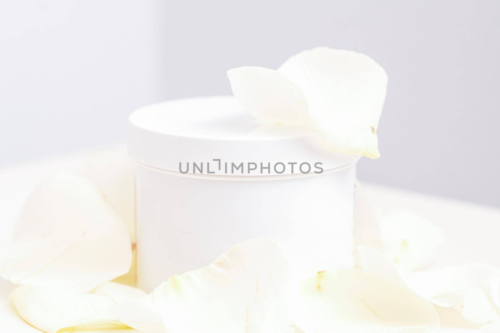 White jar with cream among delicate white rose flowers petals on a light background. Natural organic cosmetics concept, close up, mock-up