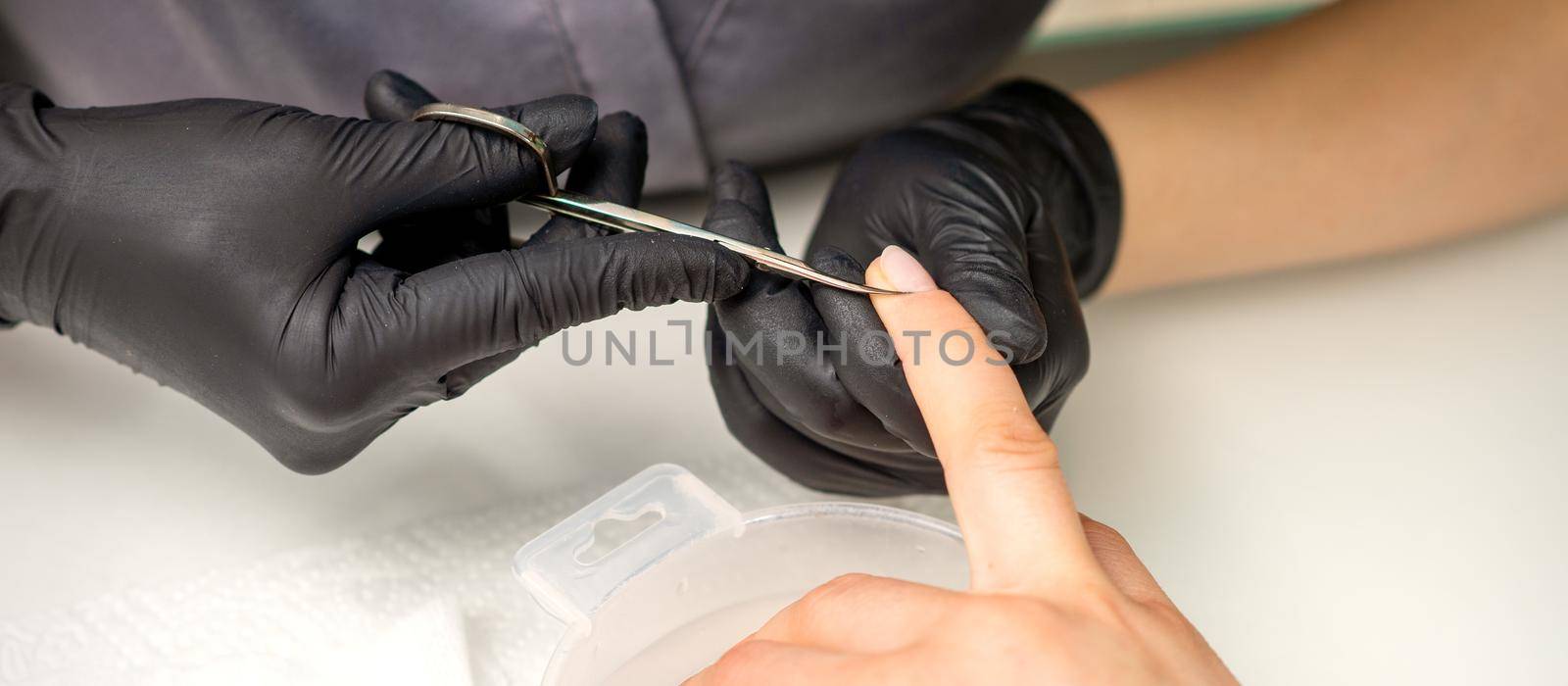 Manicure master removes cuticles from female nails with scissors wearing protective gloves in manicure salon